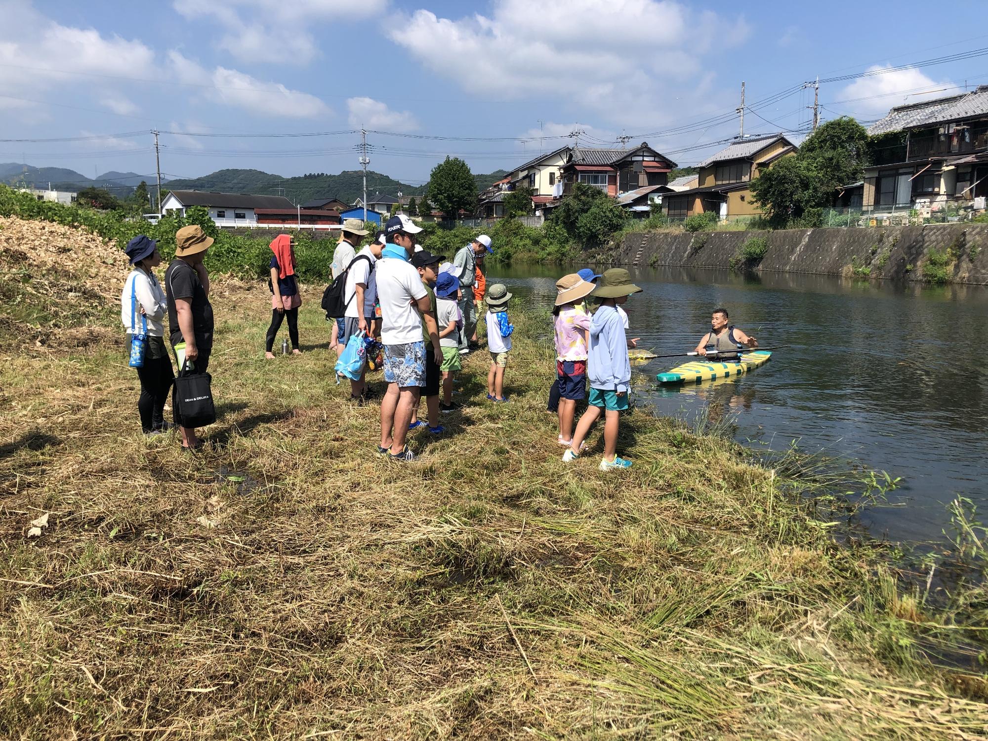 カヌー協会の男性がカヌーで川に入った様子を参加者達が岸から見ている写真