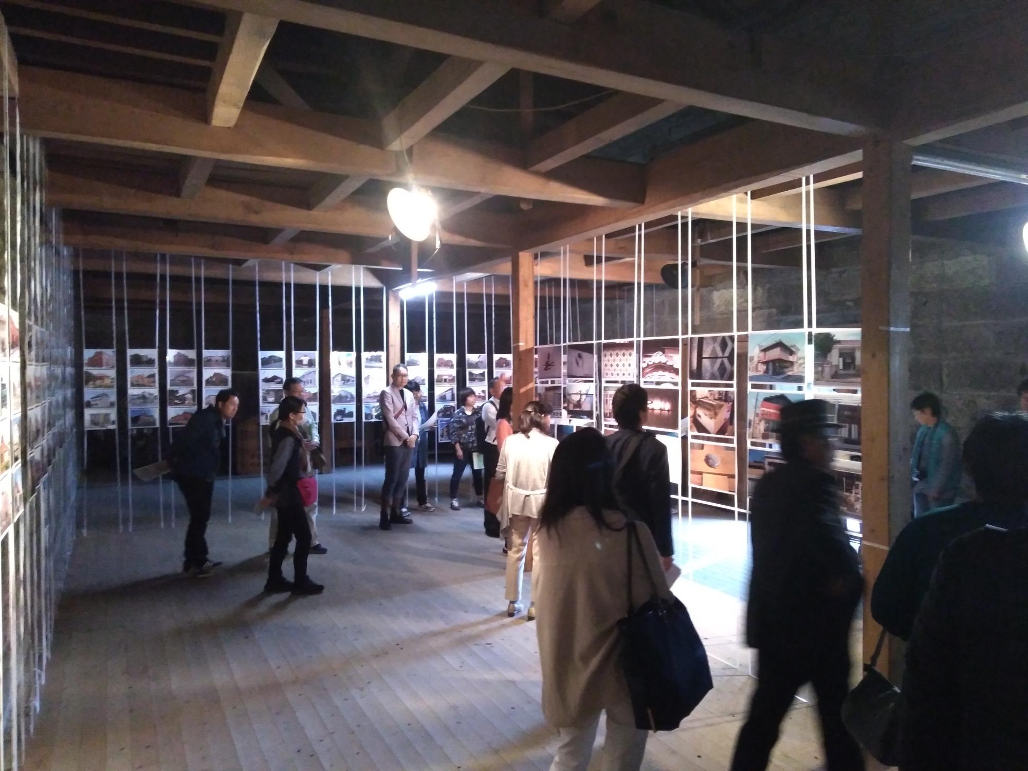 室内の壁全体に作品が飾られ天井からの照明がライトアップの効果をかもし出していてたくさんの人たちが見学している写真