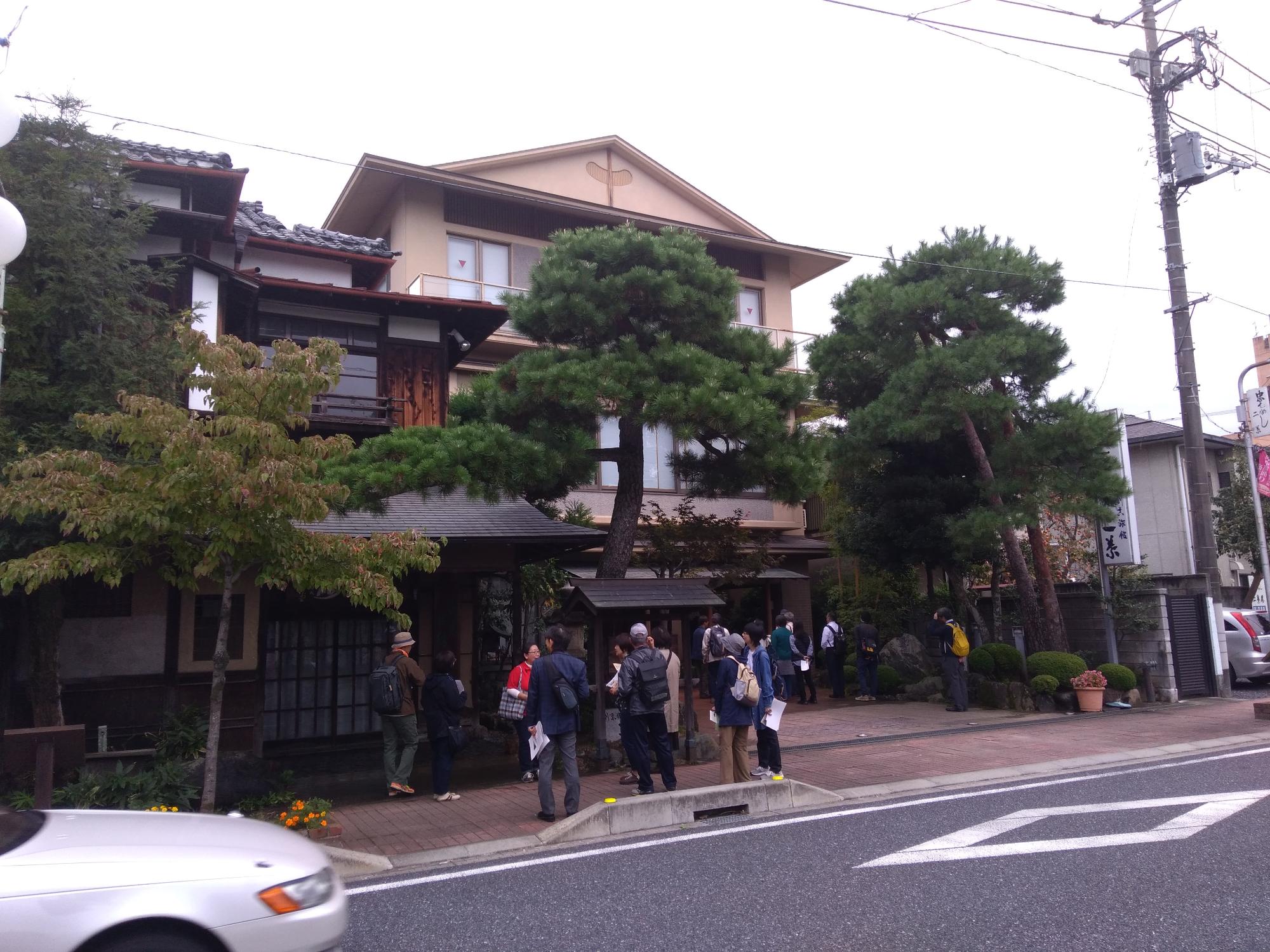 玄関脇に大きな木が立つ古めかしい構えの建物の前で見学をしている参加者の人たちの写真