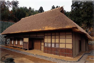 木々に囲まれた藁葺き屋根の建物で周りに砂利がしかれている吉田家住宅の外観写真