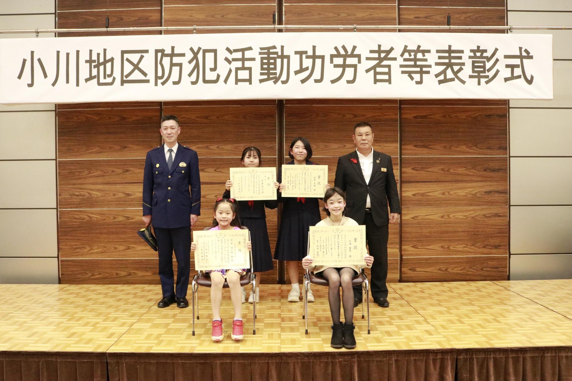 感謝状の賞状を手に持った複数のこどもたちが二人の大人と一緒に横並びに並んで記念撮影している写真