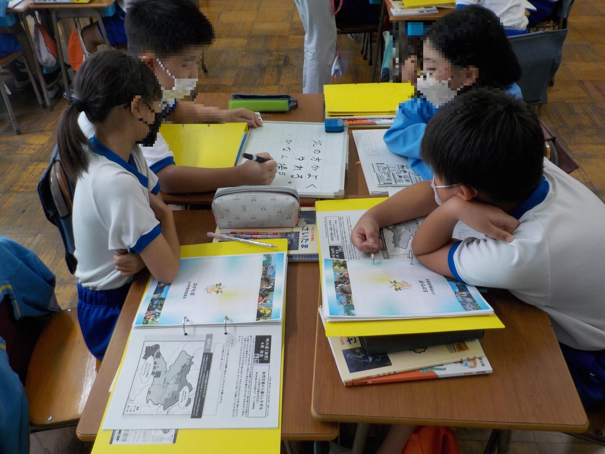グループになった小学生たちが机の上に授業のファイルを置いて話をしている写真
