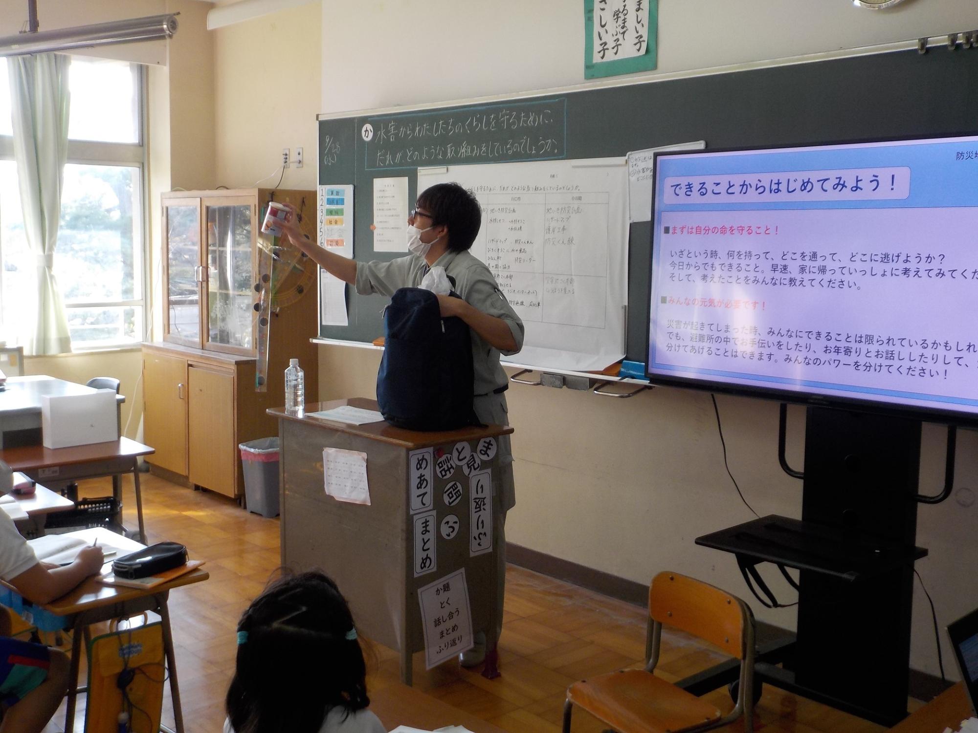 教室で男性がバッグから取り出した物を小学生に見せ話をしている写真
