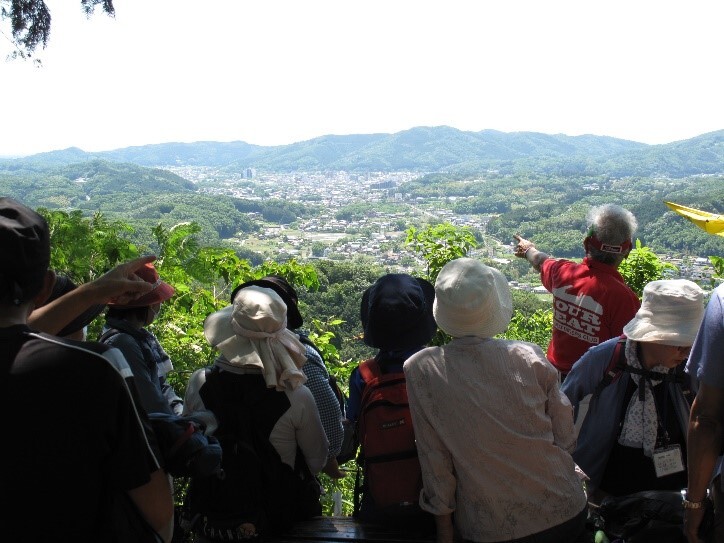 参加者たちが山から見下ろしたふもとの街並みを指さしながら見ている写真