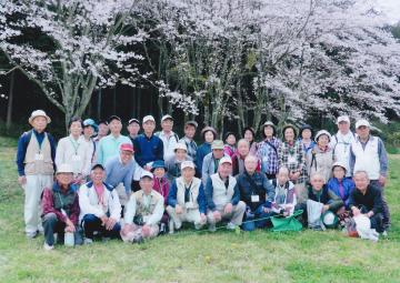 花開いた桜の木々の前で集合写真を撮る参加者たちの写真