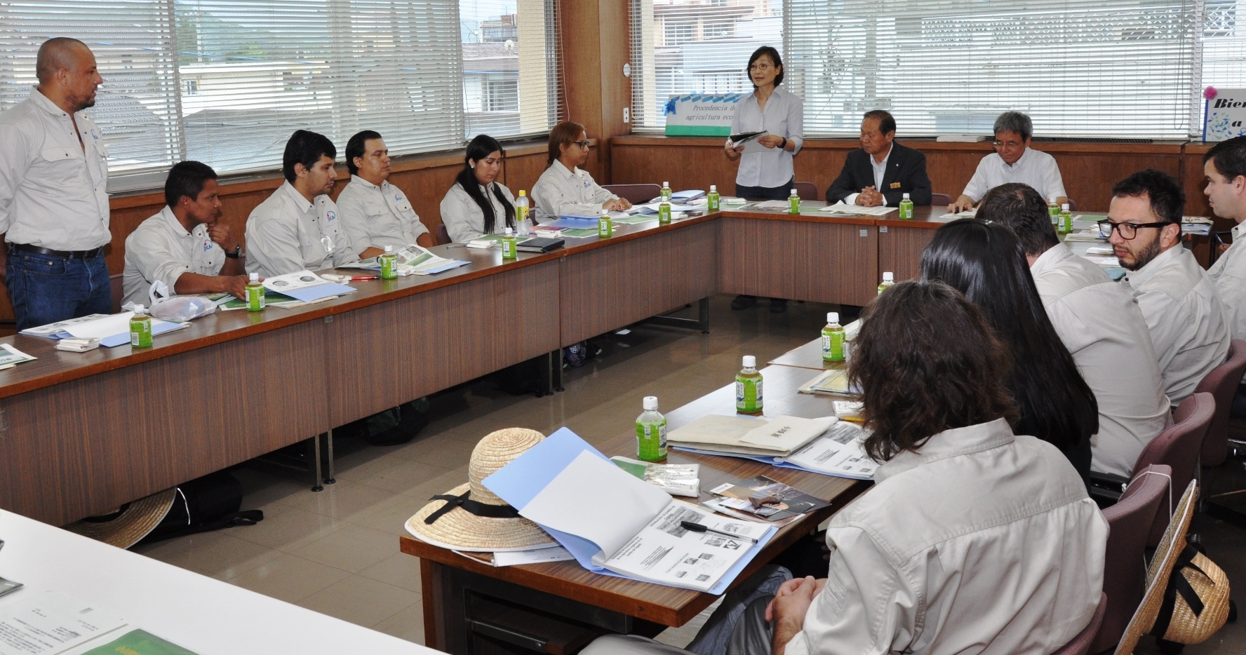 前方に座った町長の横に女性が立って話をしているのを、コの字型に設置されたテーブルと椅子に座って聞いている研修員の方々の様子を撮影した写真