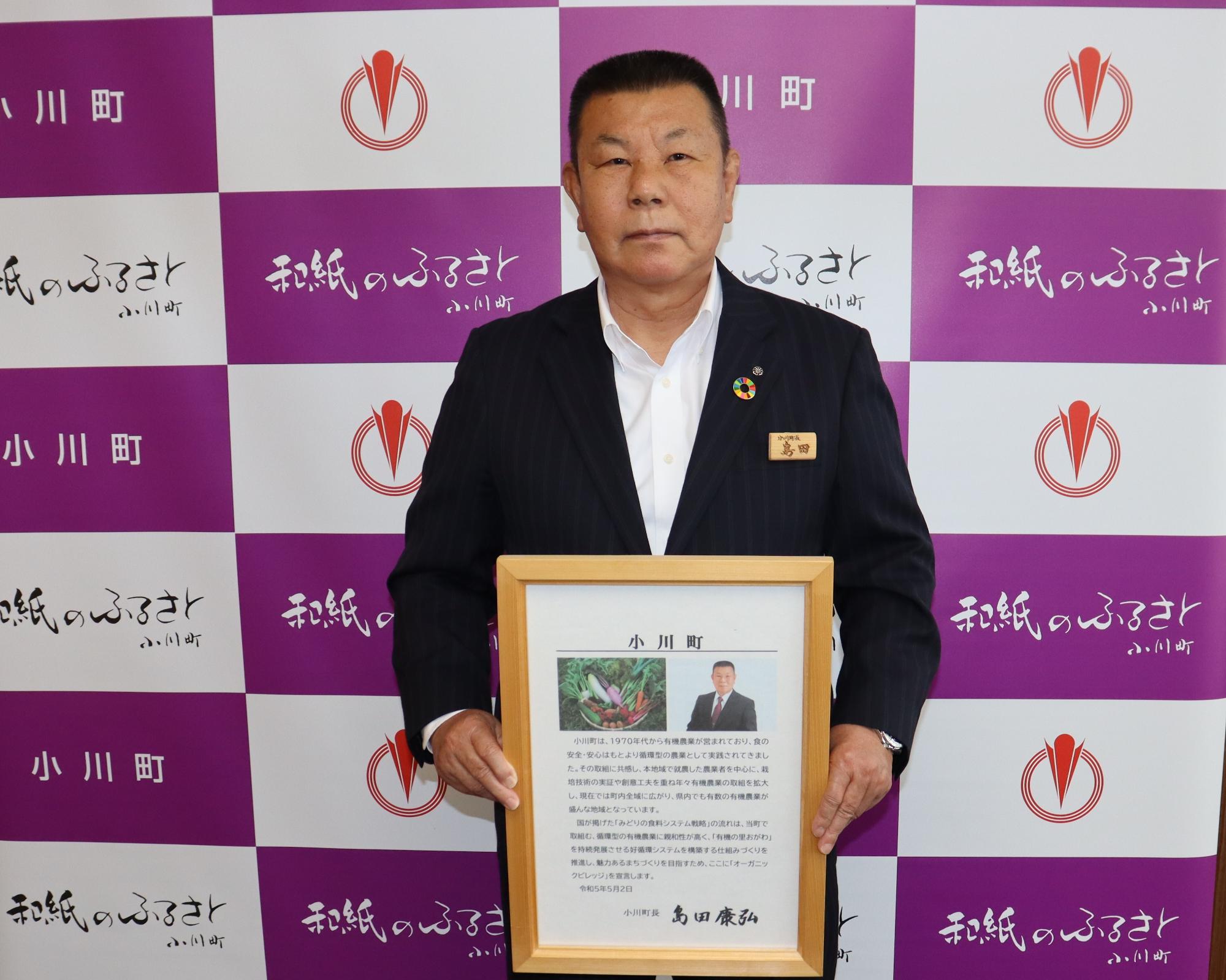 小川町のバックボードの前で賞状を両手持ち緊張したおもむきで記念撮影をしている男性の写真