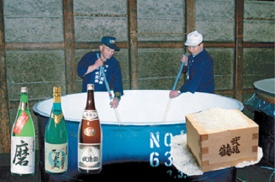 作業着姿の男性2名が大きな酒樽の中を棒のようなものでかき混ぜている写真