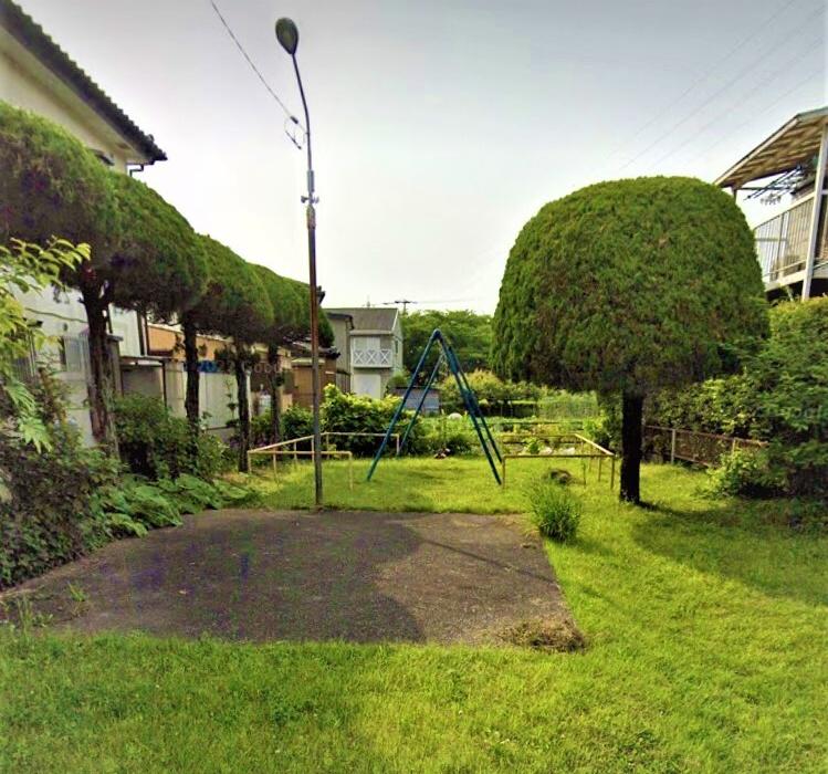 民家の間の敷地内に手入れされた木が並び、奥にブランコが設置された杉ノ木公園の写真