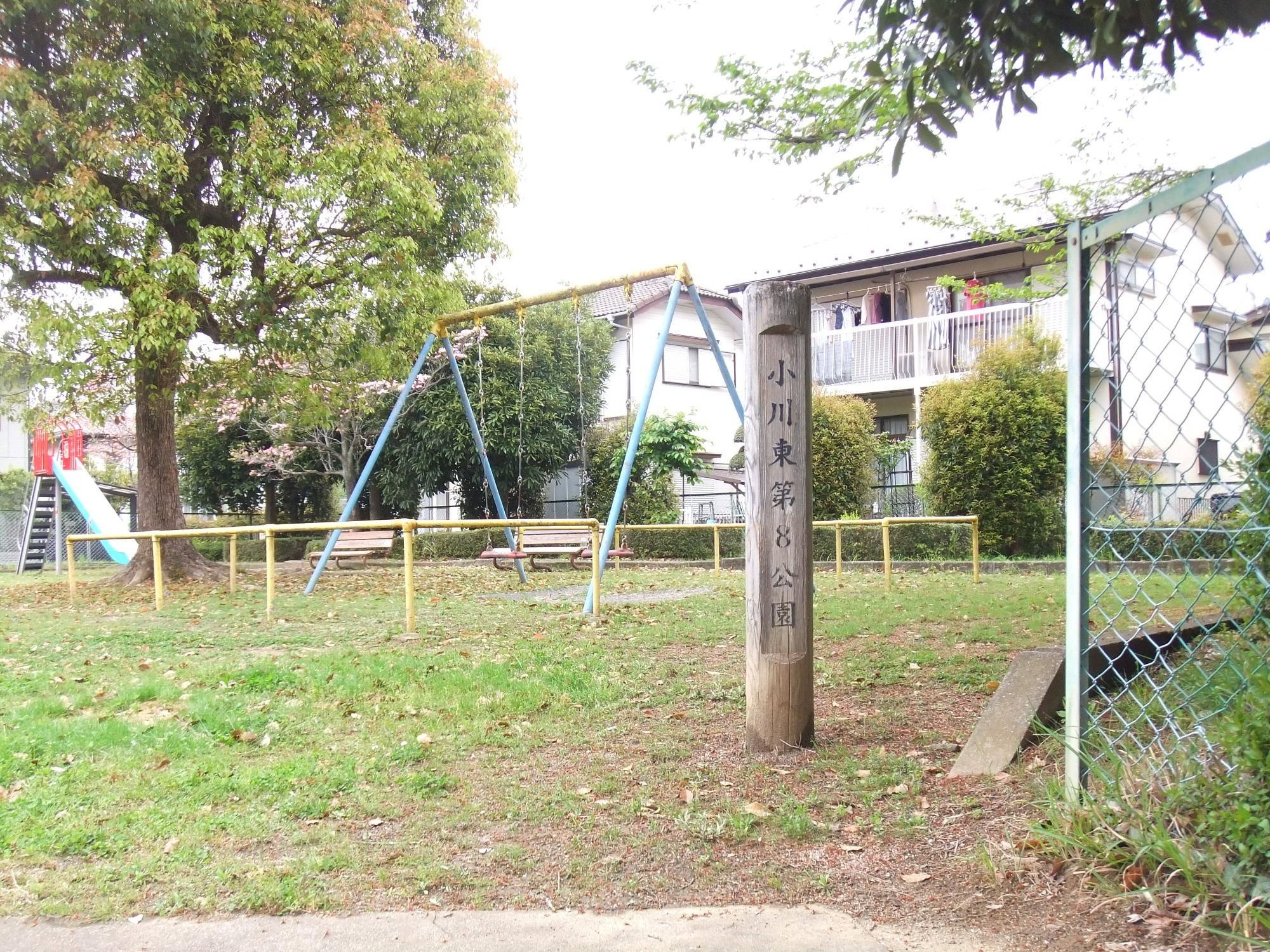 住宅街の中にあり木々や生垣に囲まれた公園内に、ブランコや滑り台などの遊具が設置された小川東第8公園の写真