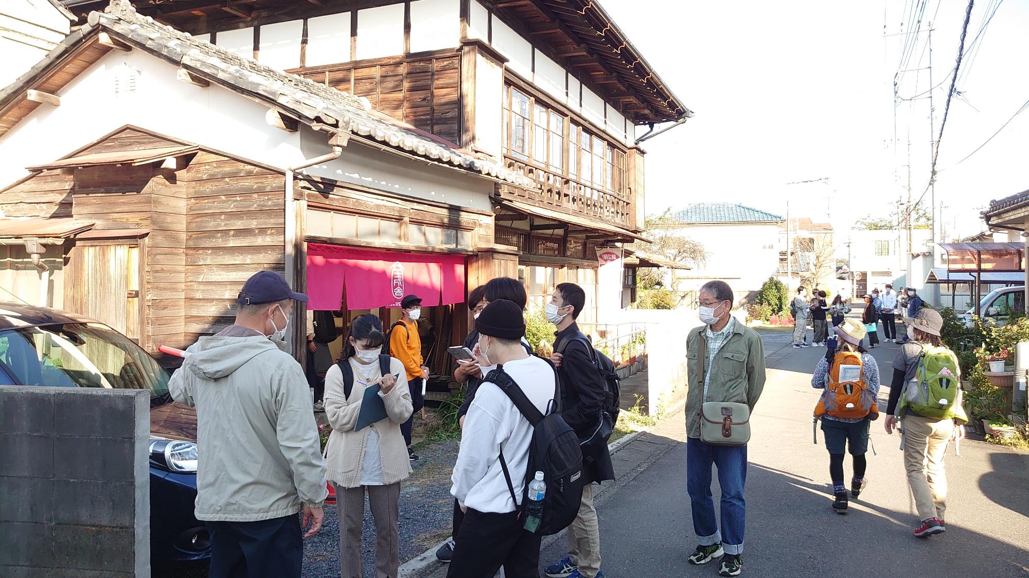 古い木造の建物の前でまち歩きの参加者がメモをとっている写真