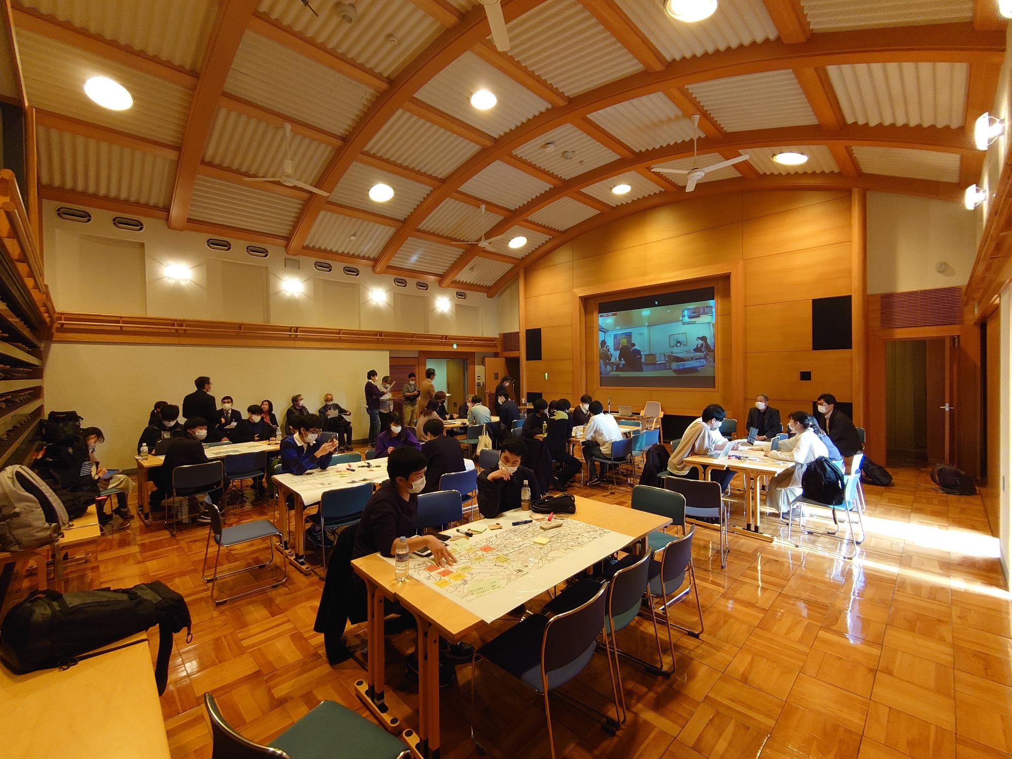 天井が高い室内にまち歩きの参加者の人たちが集まっているざわめいた室内の写真