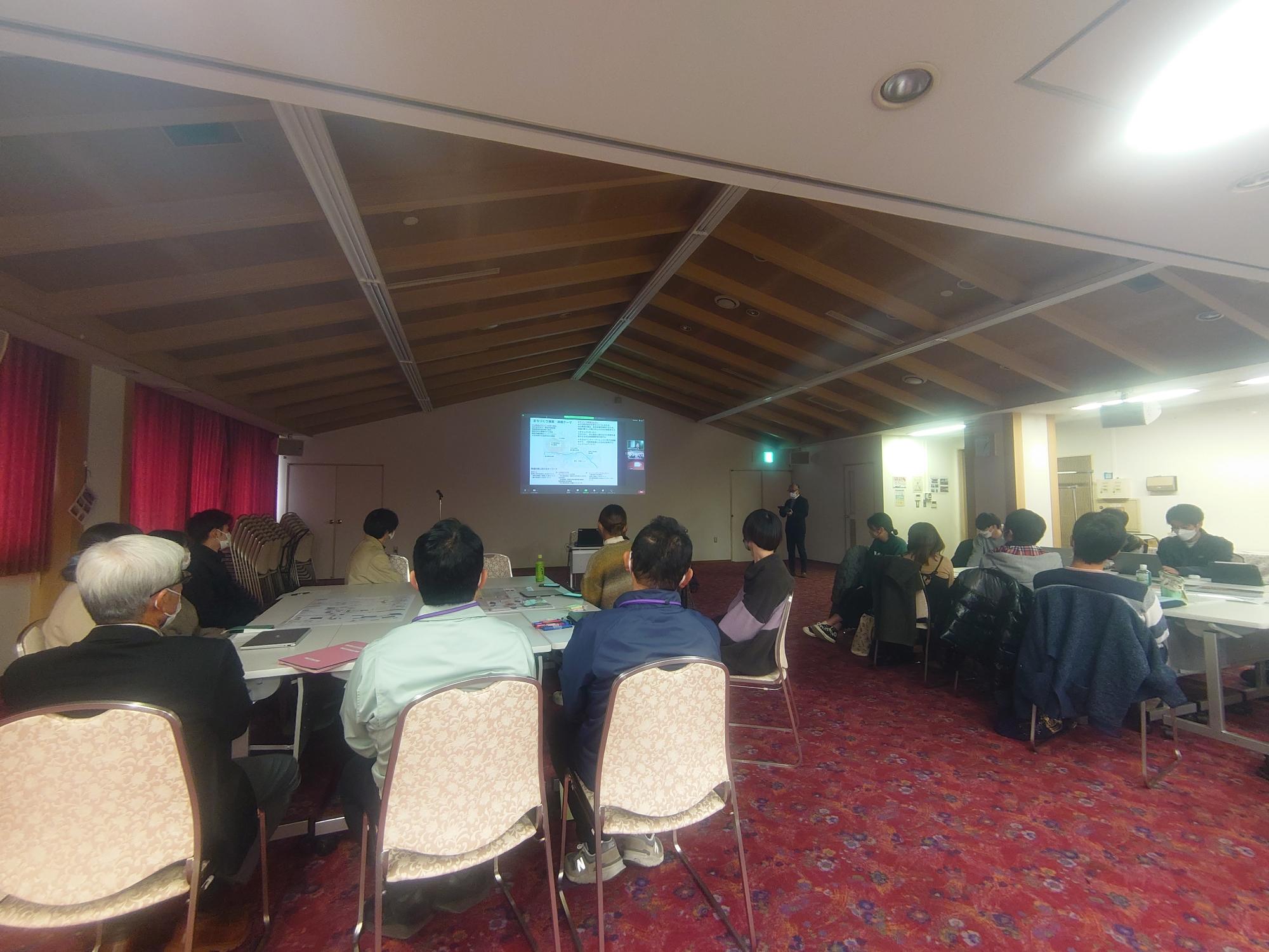 意見発表会の会場で前方のスクリーンを見ている参加者の人たちの広報から全体を写した写真