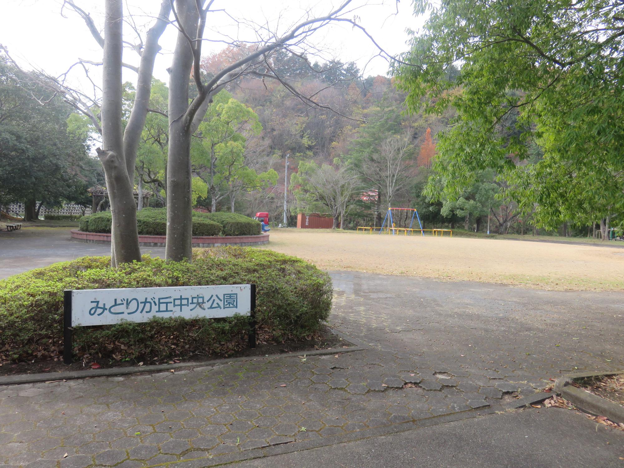 背の低い植栽と、大きな2本の木が植えられている根元に「みどりが丘中央公園」と書かれた園名版が設置されている公園入口付近の写真
