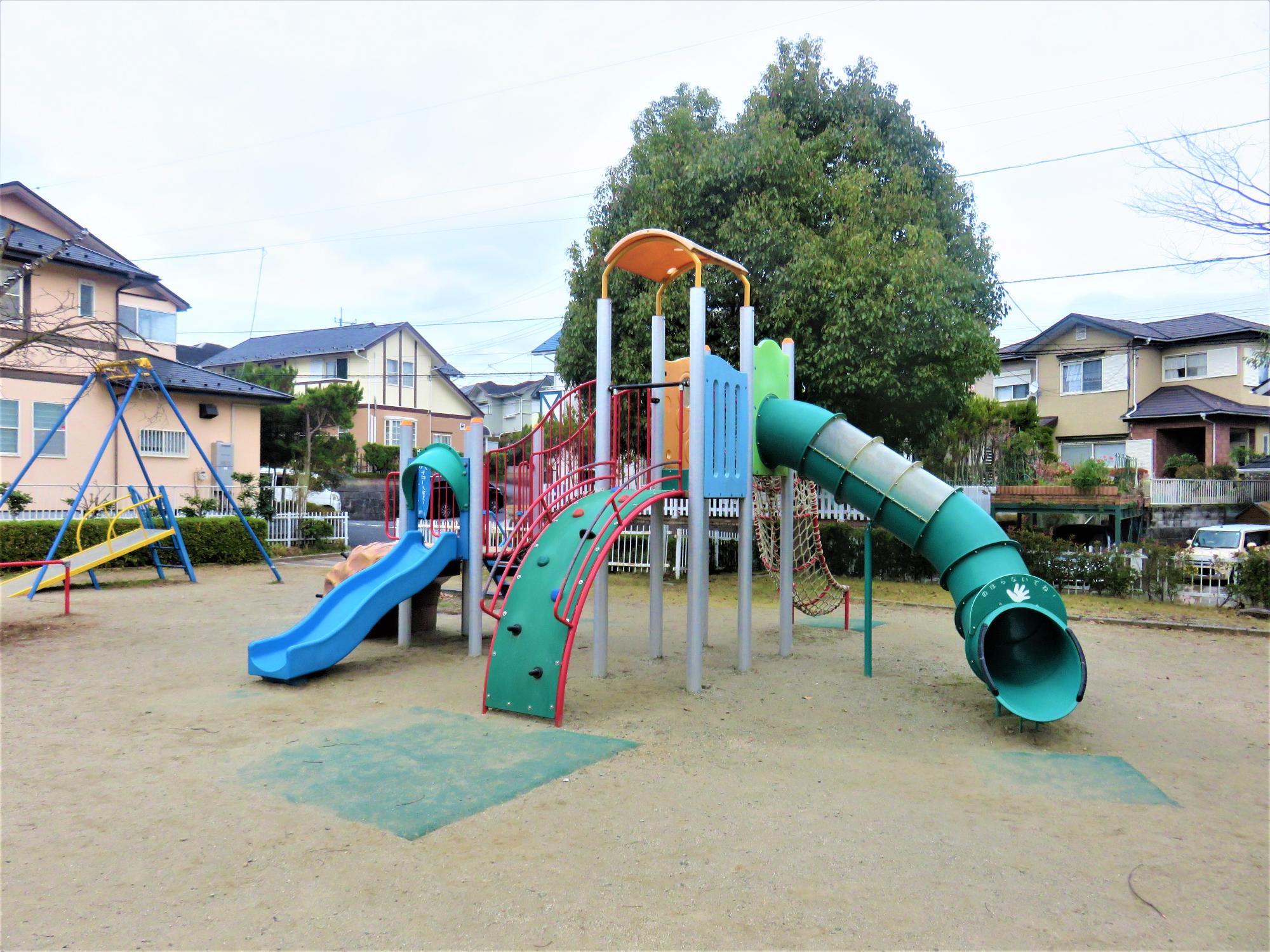 水色の滑り台、トンネル状になっている滑り台、ネットなどが付いている複合遊具の写真