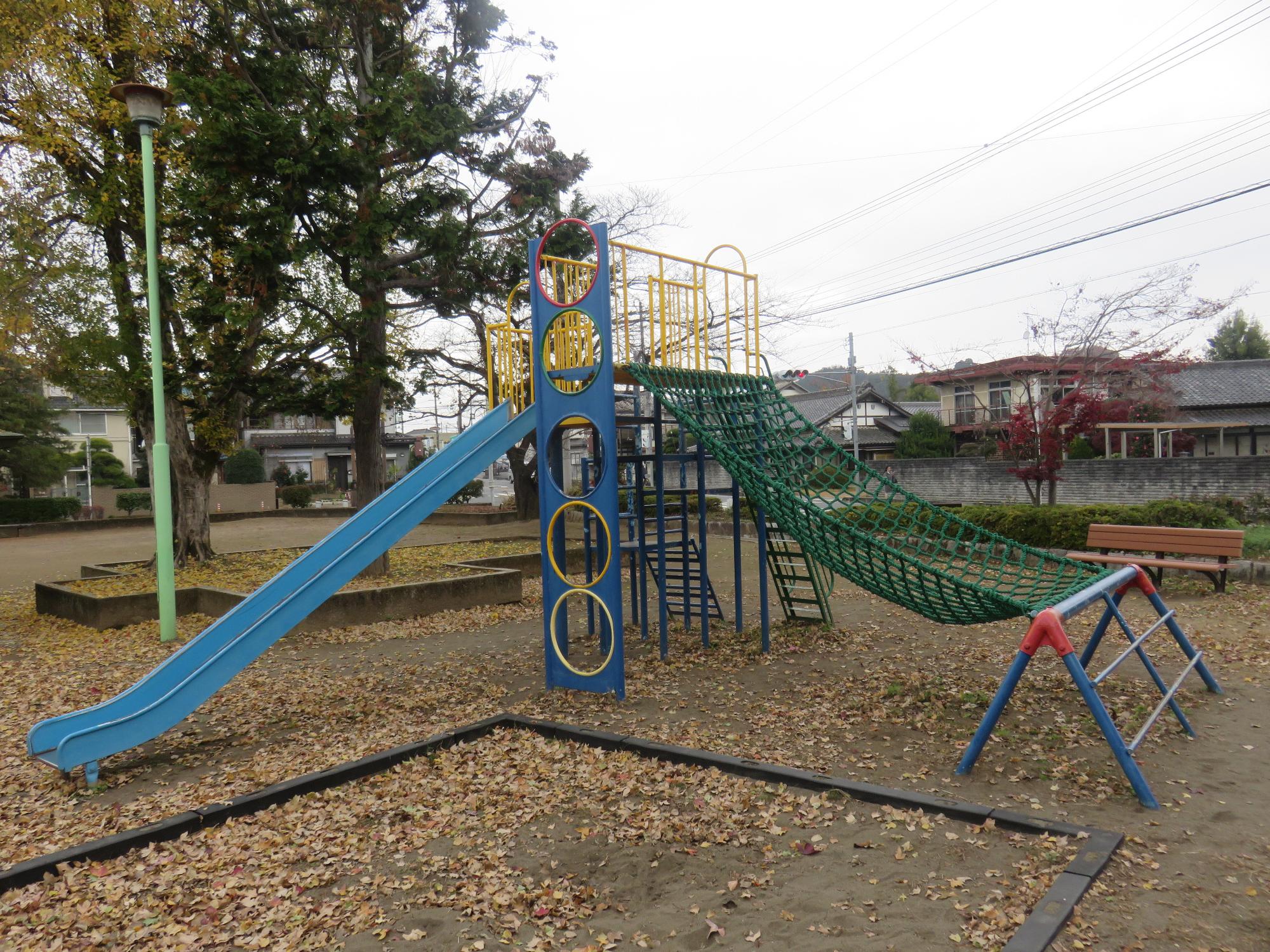 砂場の横に設置されている、滑り台や緑色のネットが付いた複合遊具の写真