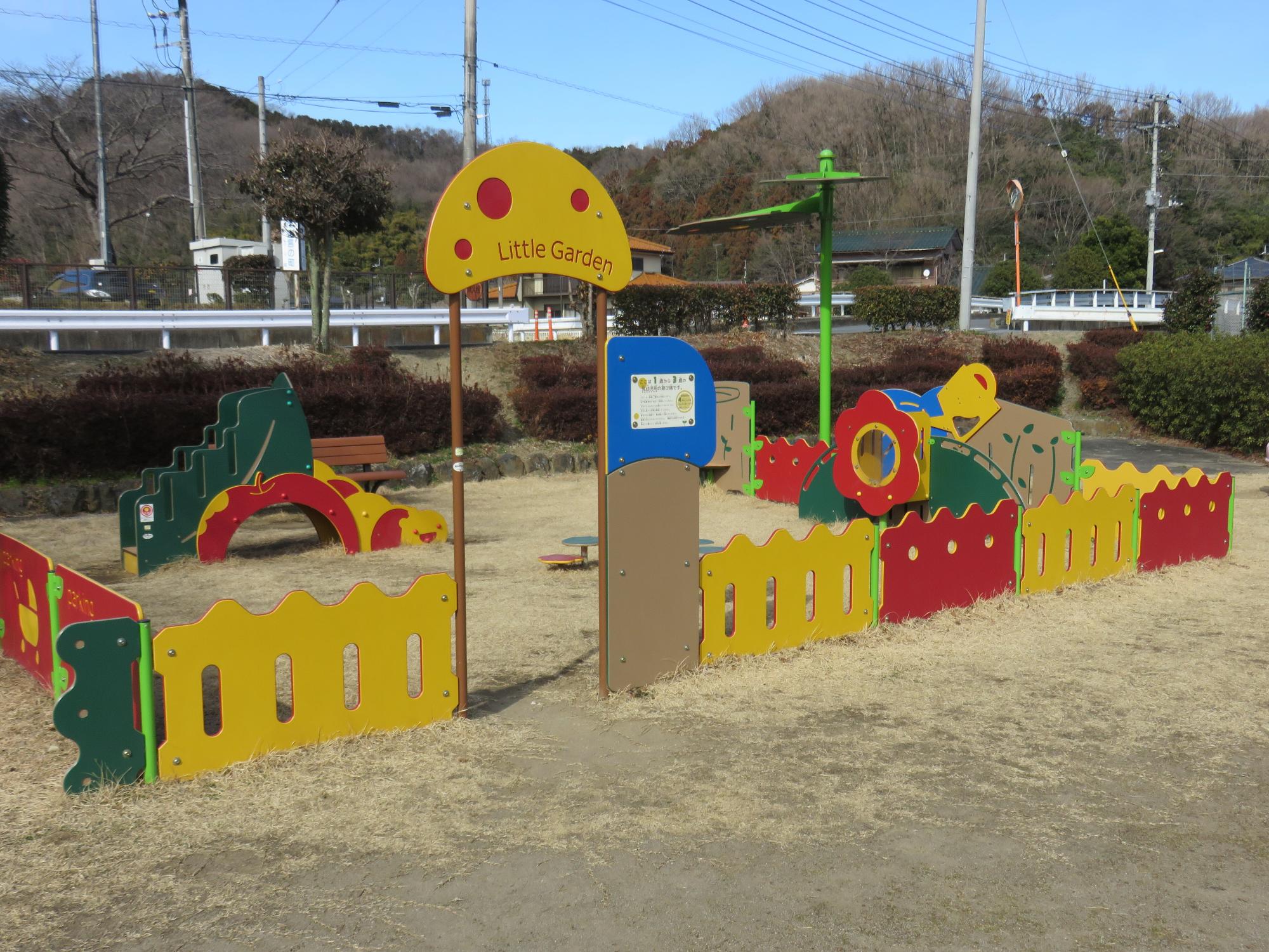 周りを背の低い柵が囲んだ中に、赤や黄色、緑色などが使われた乳幼児用遊具が設置されている公園内一角の写真