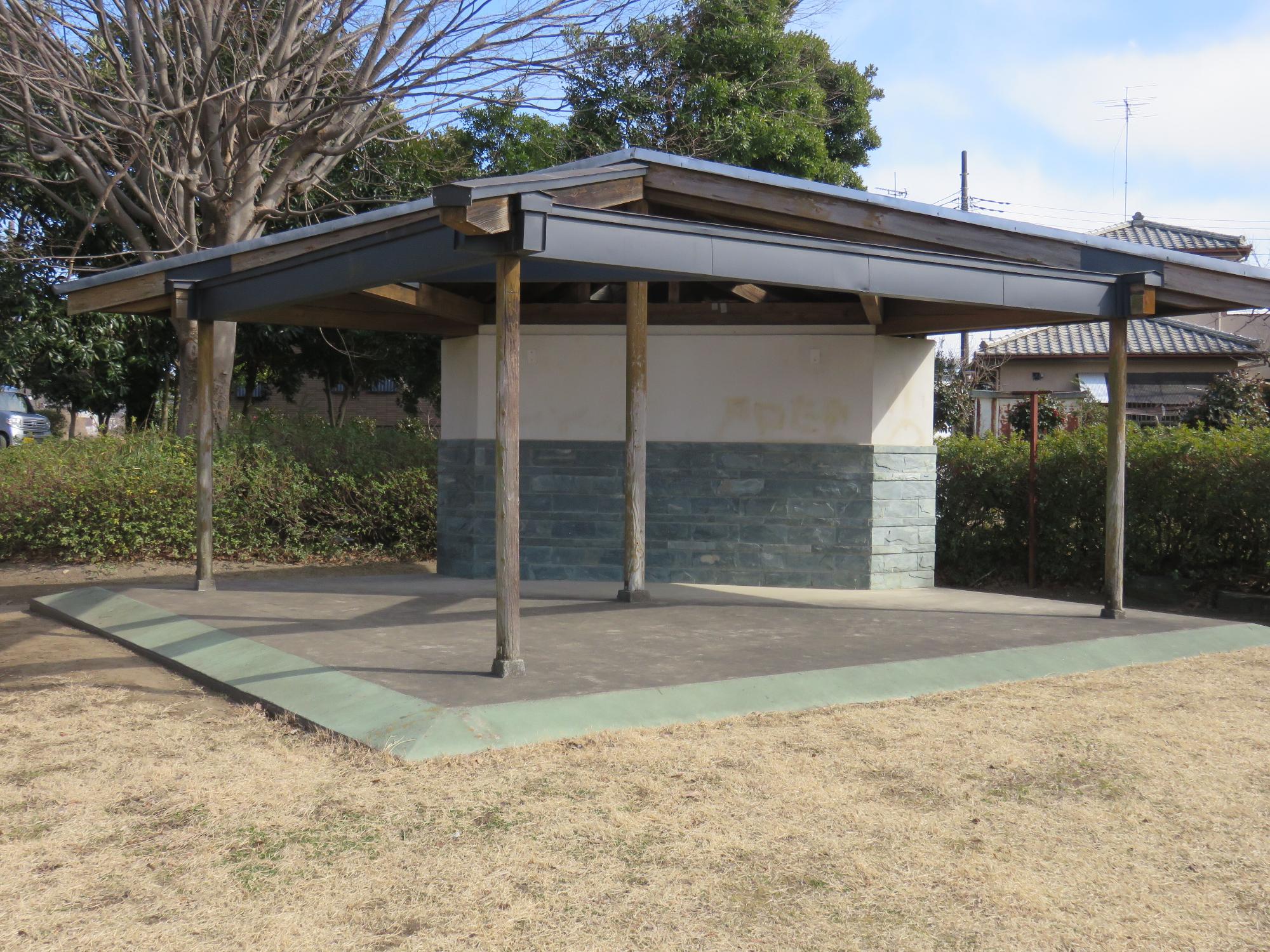 三角形のような形をしたコンクリート造りの地面の奥に建っているトイレの外観を写した写真