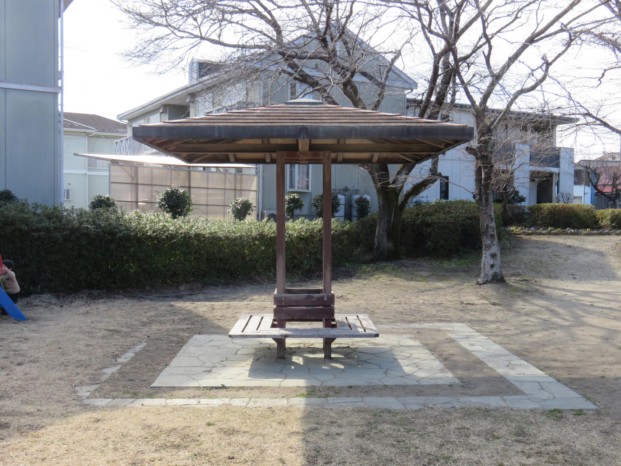 芝生の一部にタイルが敷かれ、屋根の下にはベンチが設置されている東屋の写真