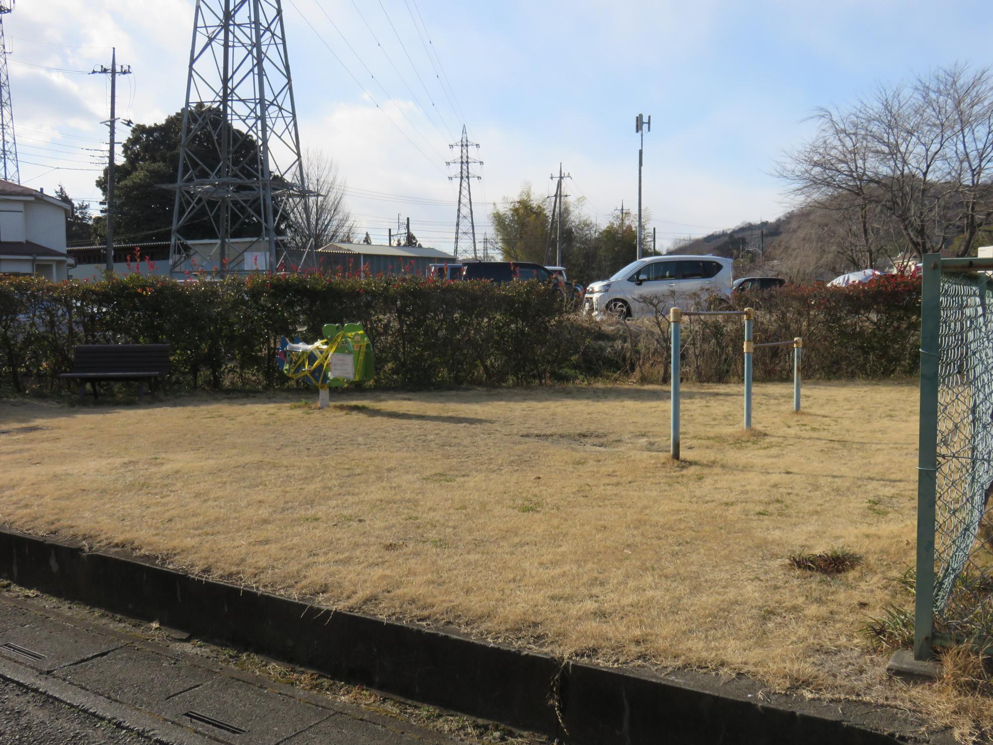 近くに鉄塔があり生垣やフェンスで囲まれた敷地内にベンチや鉄棒が設置された通木公園の写真