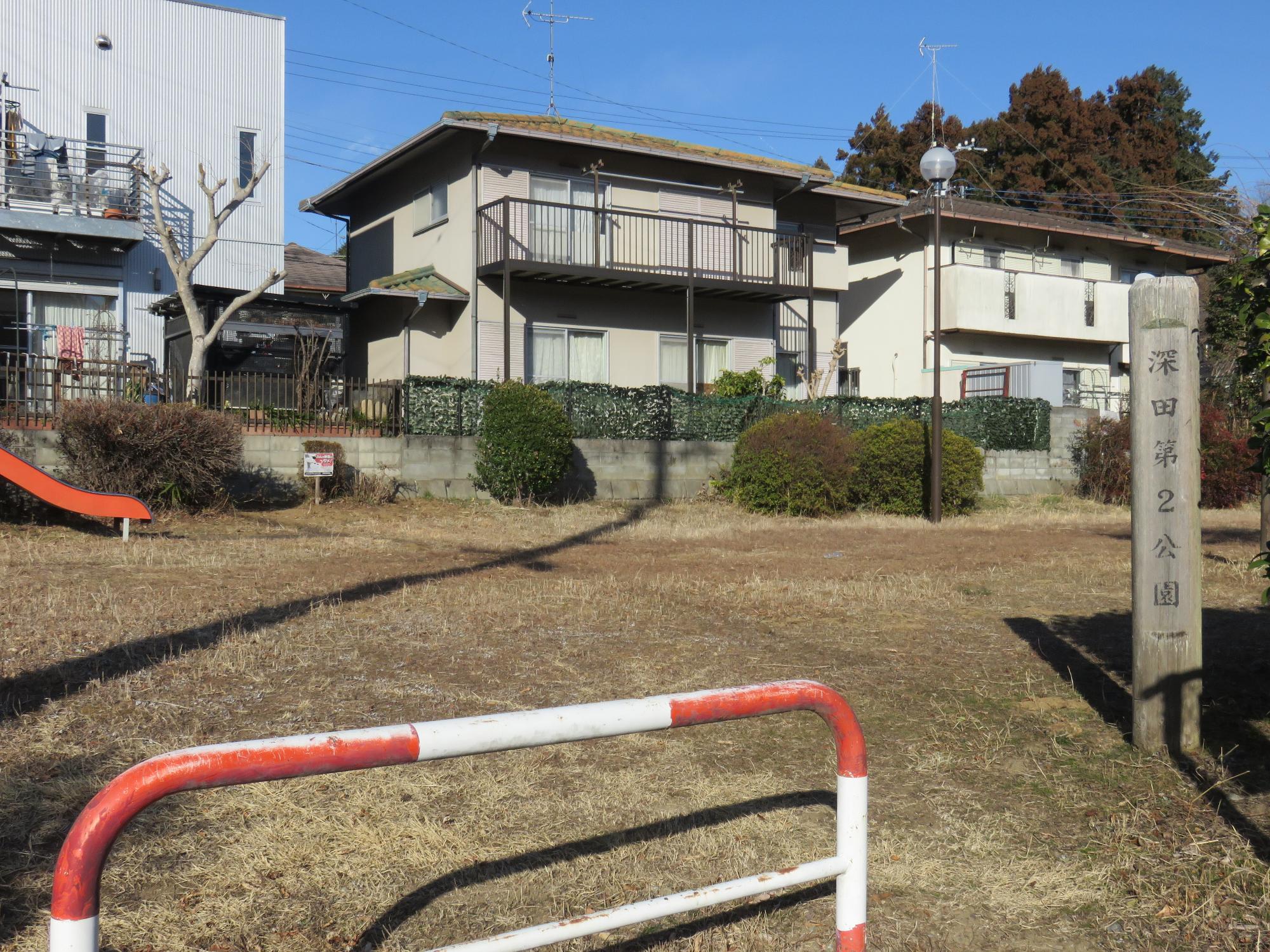 住宅街に隣接した敷地内に生垣や街灯、すべり台が設置された深田第2公園の写真