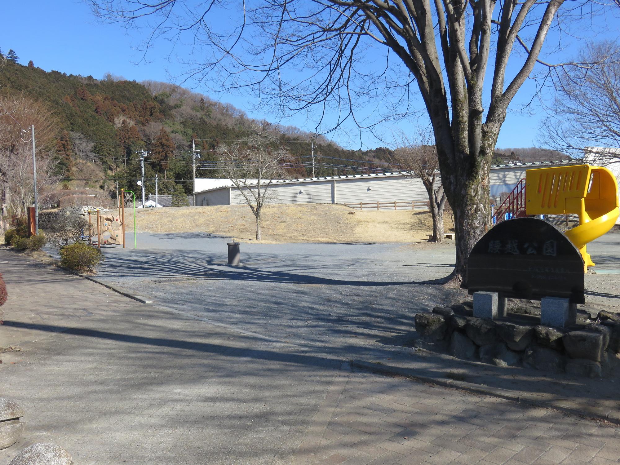 「腰越公園」と書かれた園名版の奥に滑り台、築山などが見える腰越公園の写真