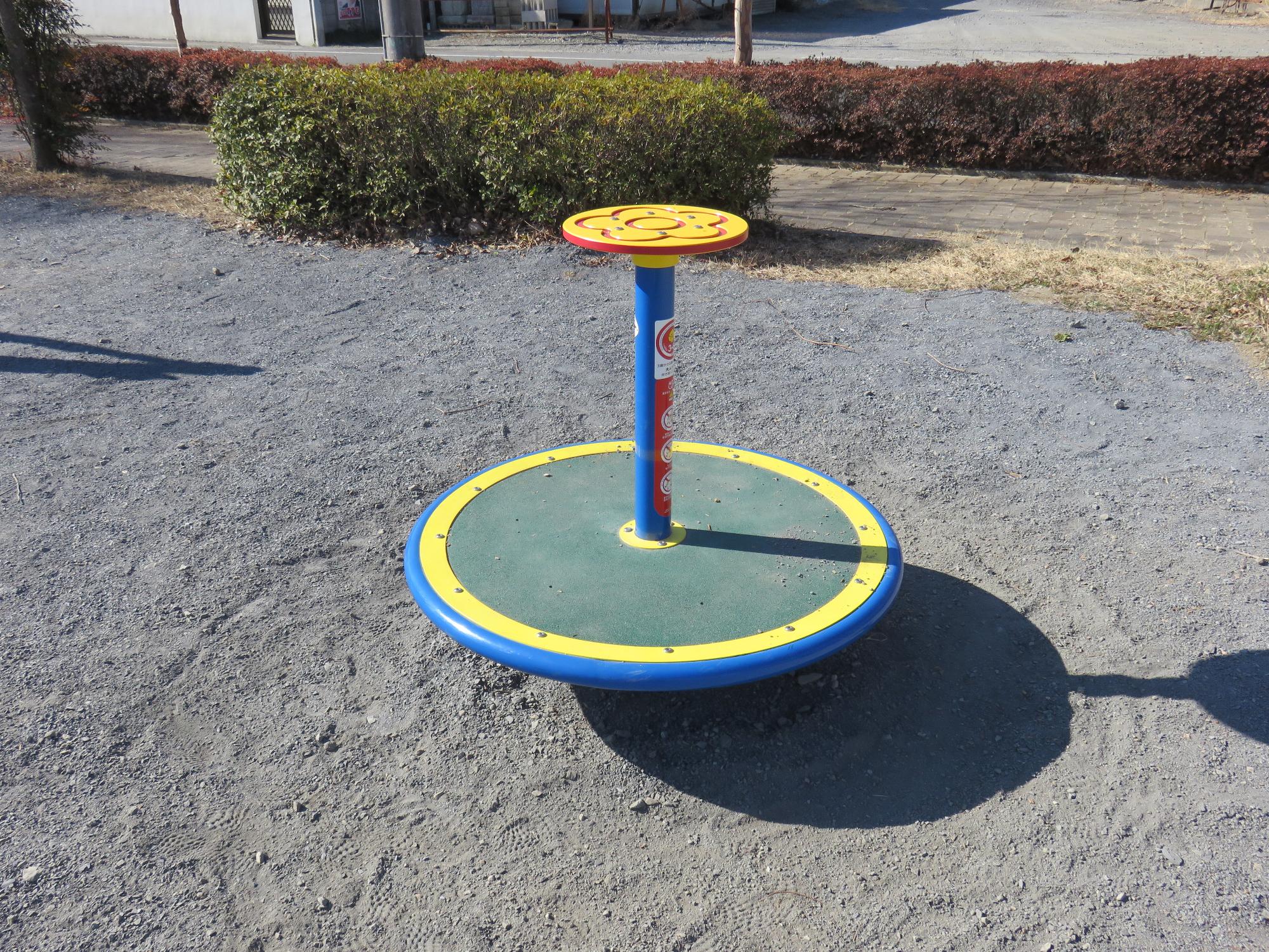 下部分に大きめの円盤状の土台、土台の中心に1本の支柱があり支柱の上には小さい円盤が付いている回転遊具の写真