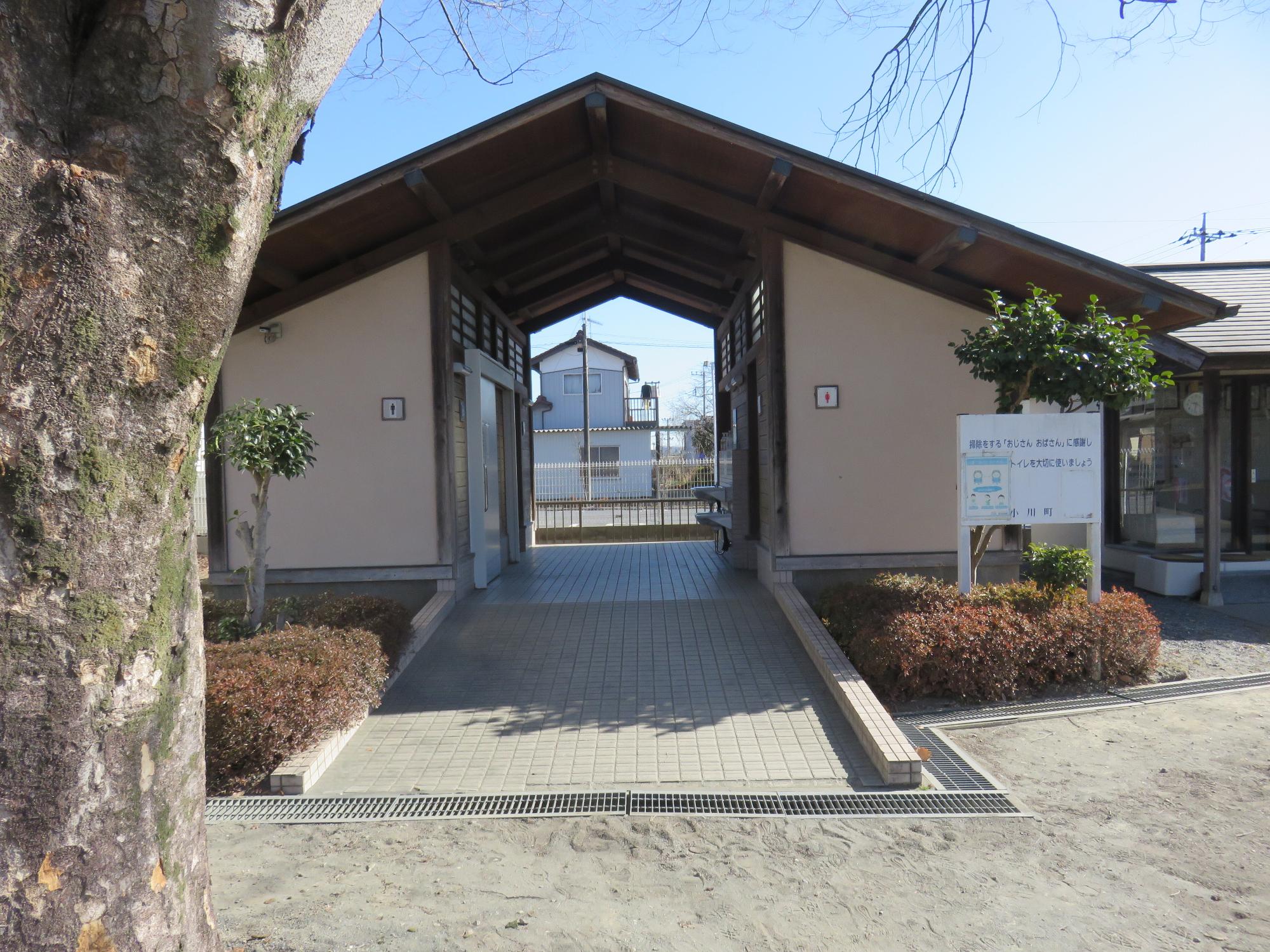 トイレに向かってスロープが伸び、左側が男子トイレ、右側が女子トイレになっている三角屋根をしたトイレの外観写真