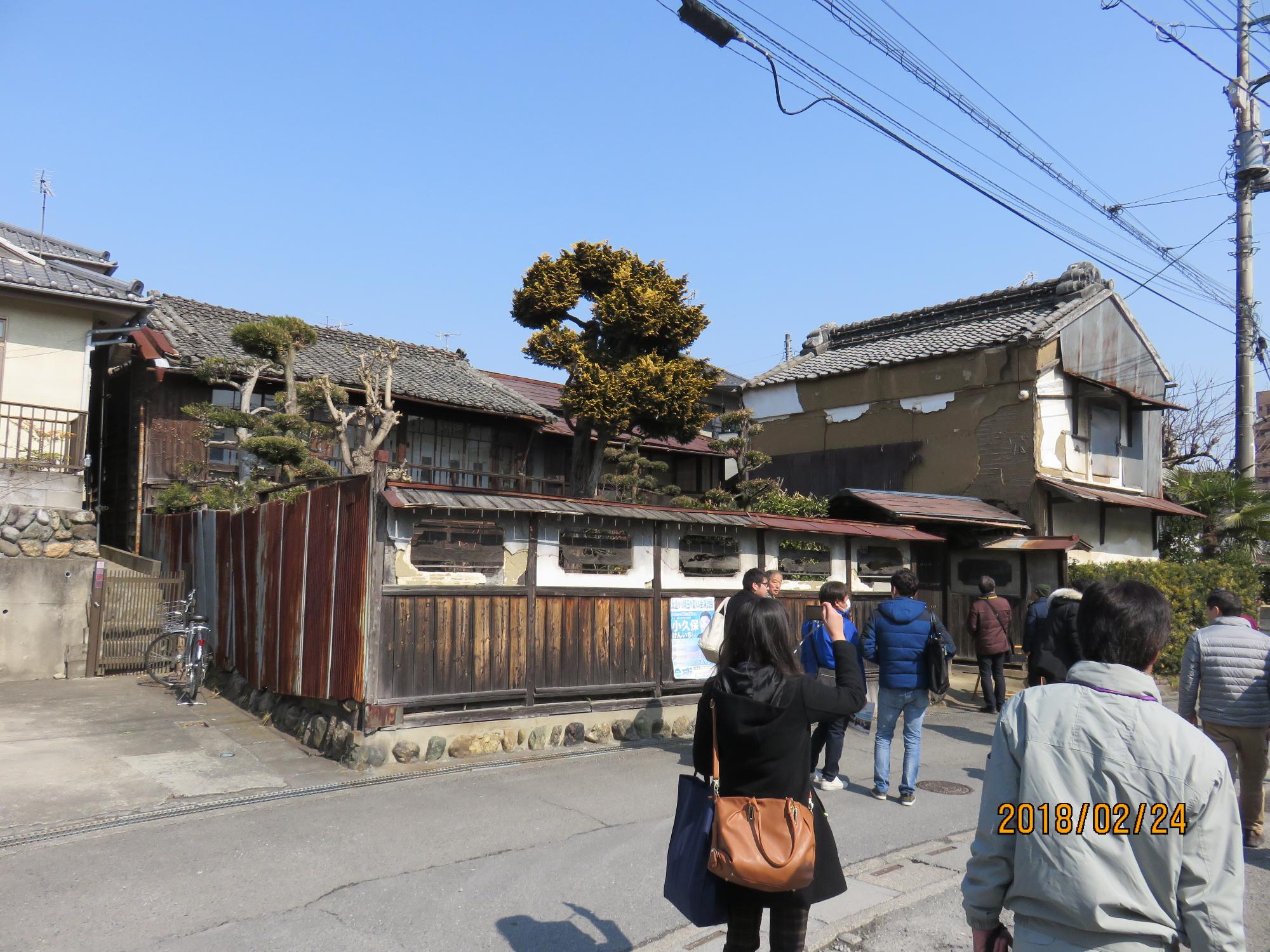 和風の造りをした塀と、その奥に建っている趣のある家の前で参加者達が写真を撮ったりなどしている写真