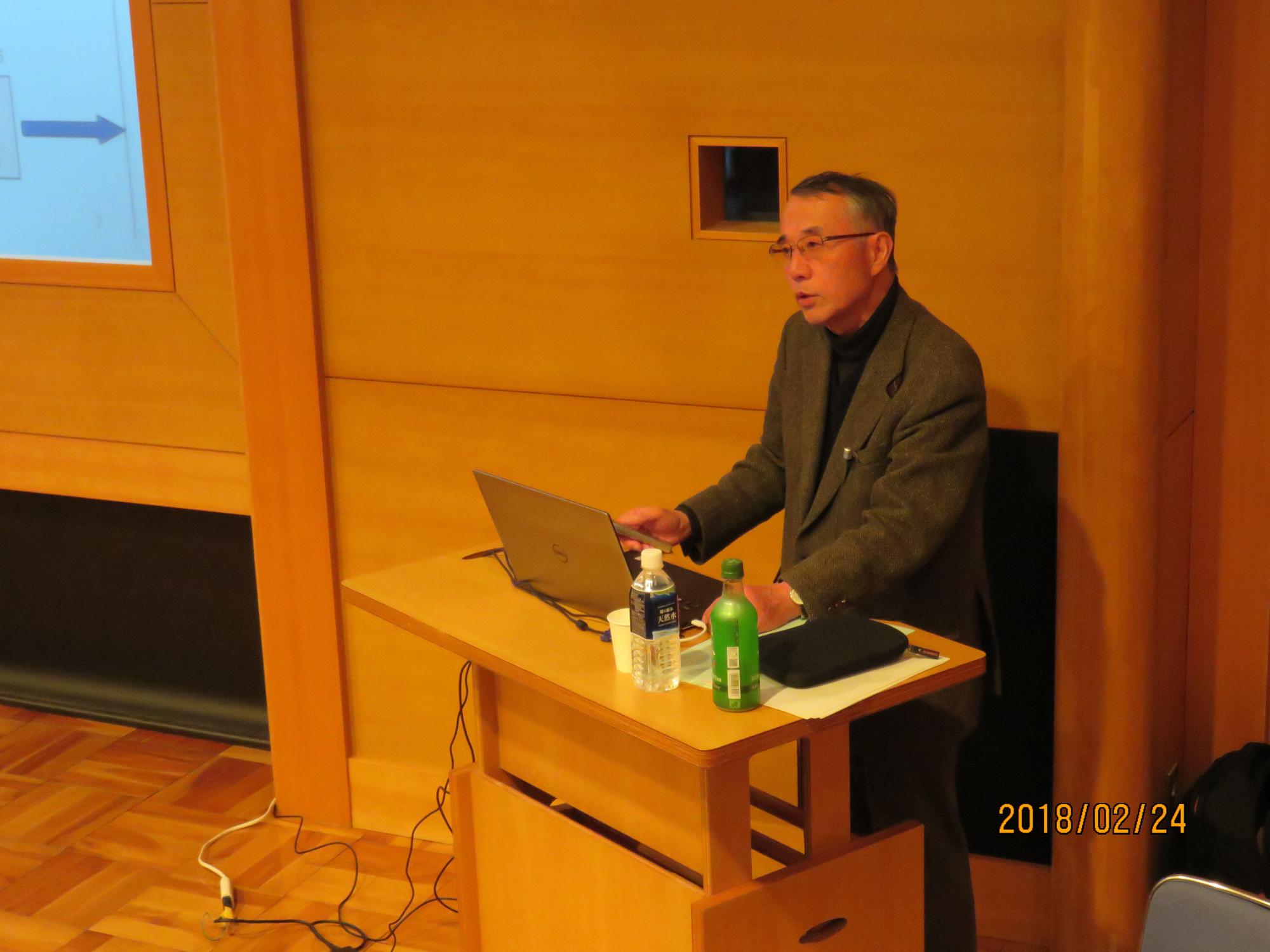 演台に立ち、ノートパソコンを開いて講演を行っている苅谷氏の写真