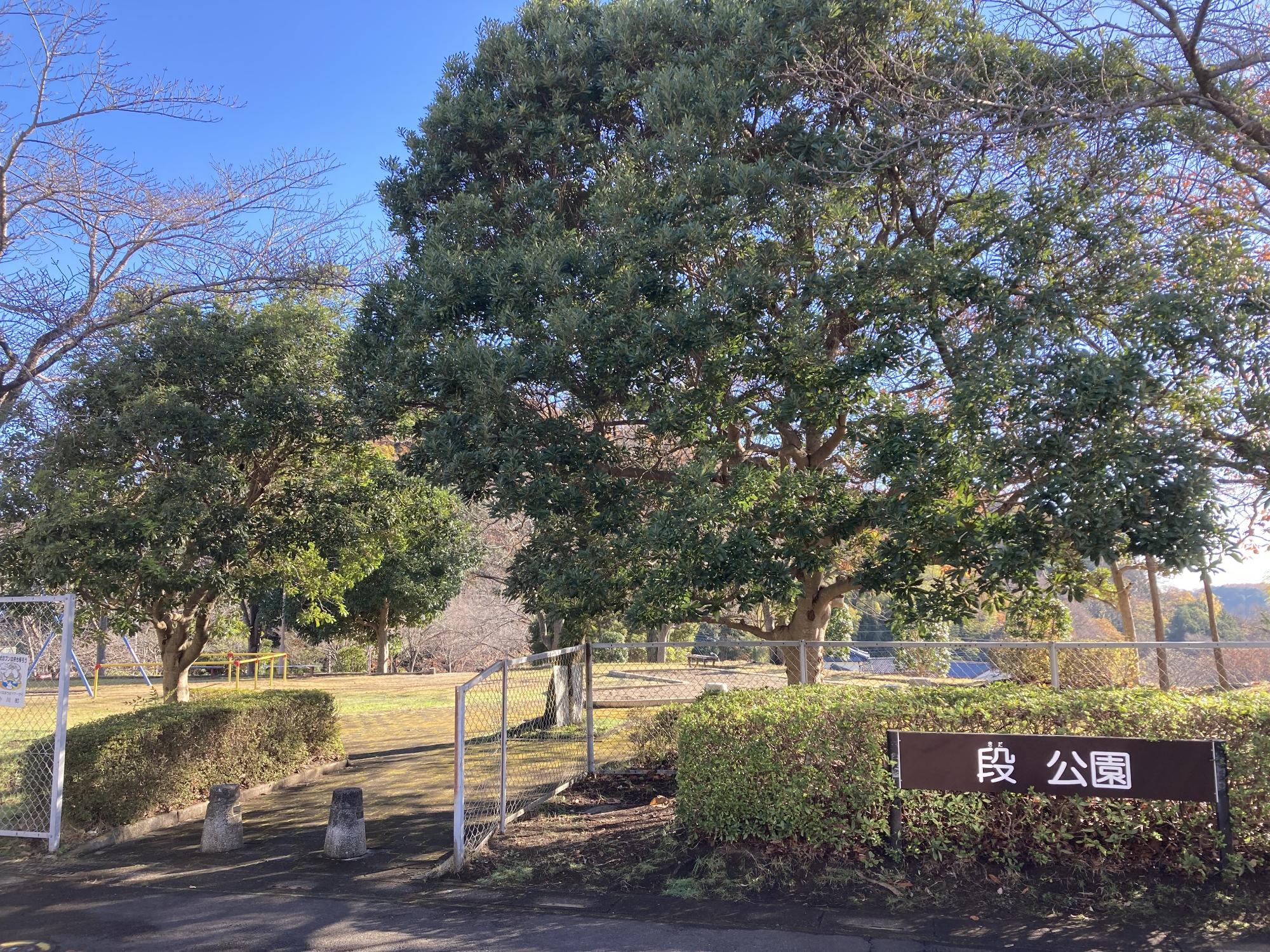 フェンスと木々や生垣に囲まれた敷地内にブランコや砂場が設置されたみどりが丘段公園の写真