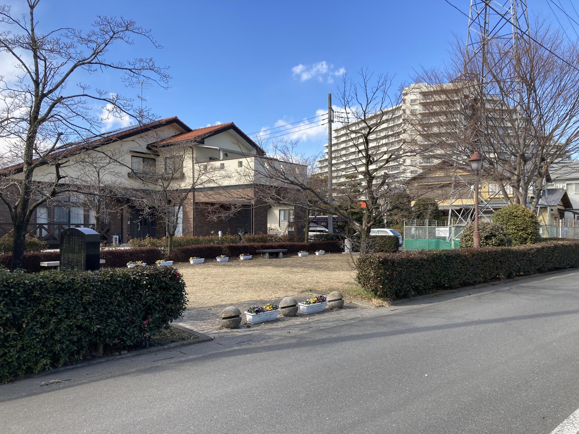 住宅街の一角の敷地内を生垣に囲まれ、ところどころ木々が生えベンチが設置された小川南公園の写真