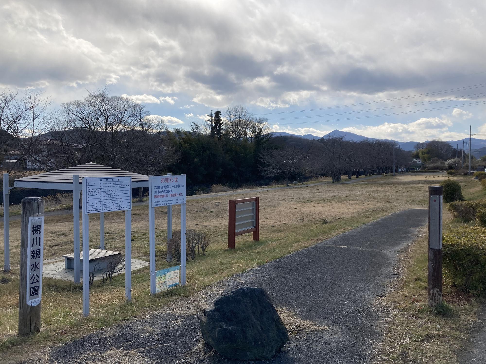 木々が真っすぐに立ち並ぶ敷地内に東屋が設置された槻川親水公園の写真