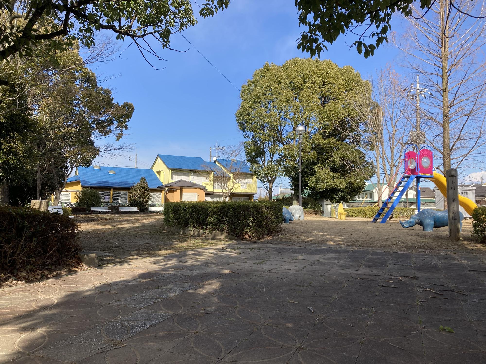 大きな木や生垣に囲まれた公園内に、すべり台やカバの形をした象形遊具が整備された小川東第7公園の写真