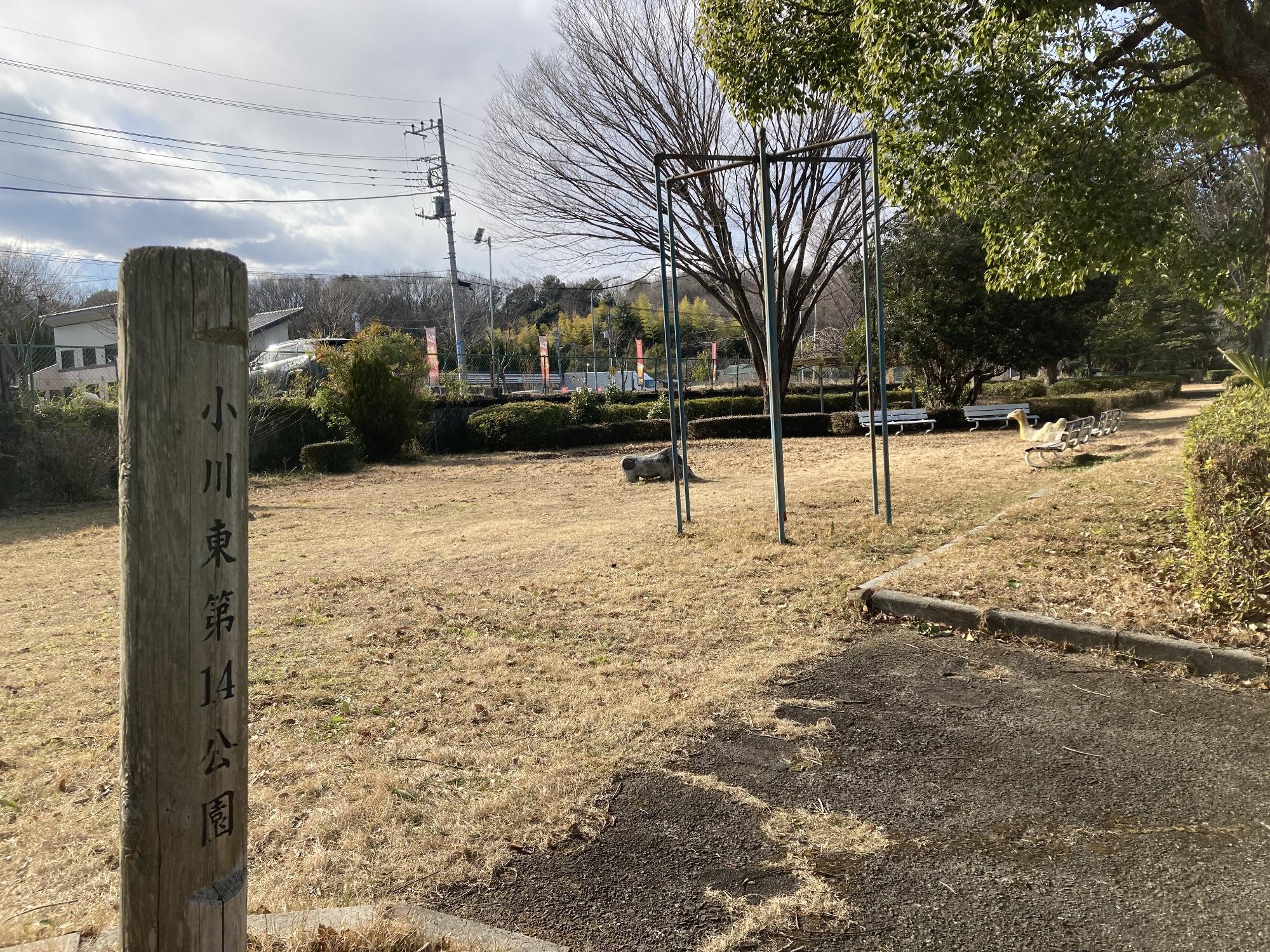 生垣に囲まれた公園内に、2台のベンチとはんとう棒や象形遊具などの遊具が整備された小川東第14公園の写真