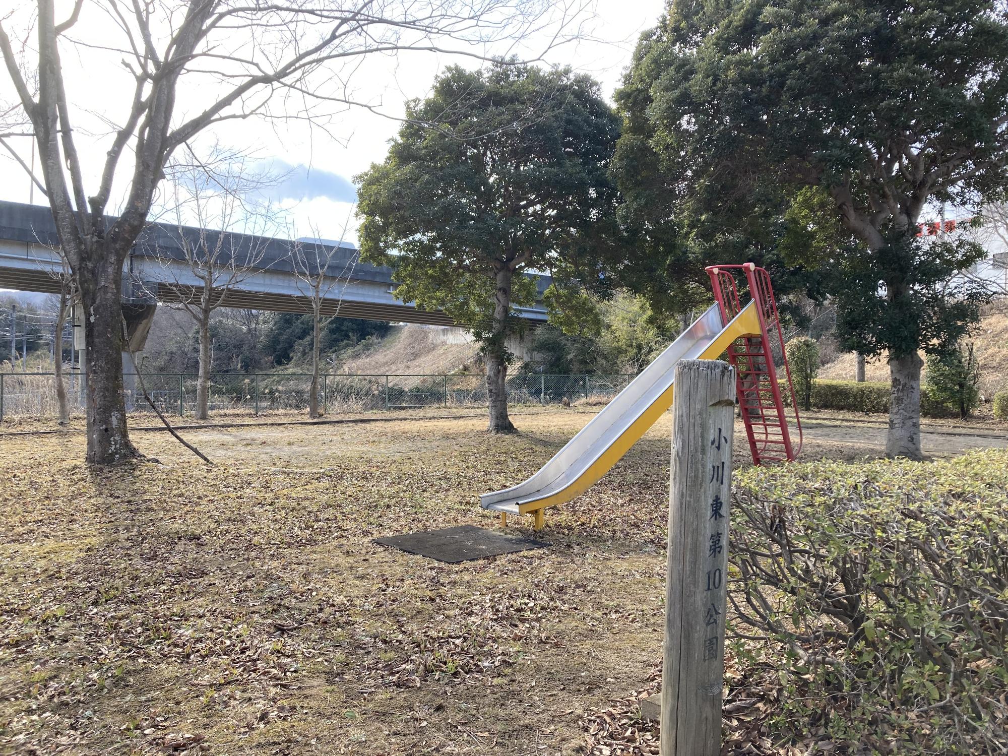 木々に囲まれた公園の中央にすべり台が設置された小川東第10公園の写真