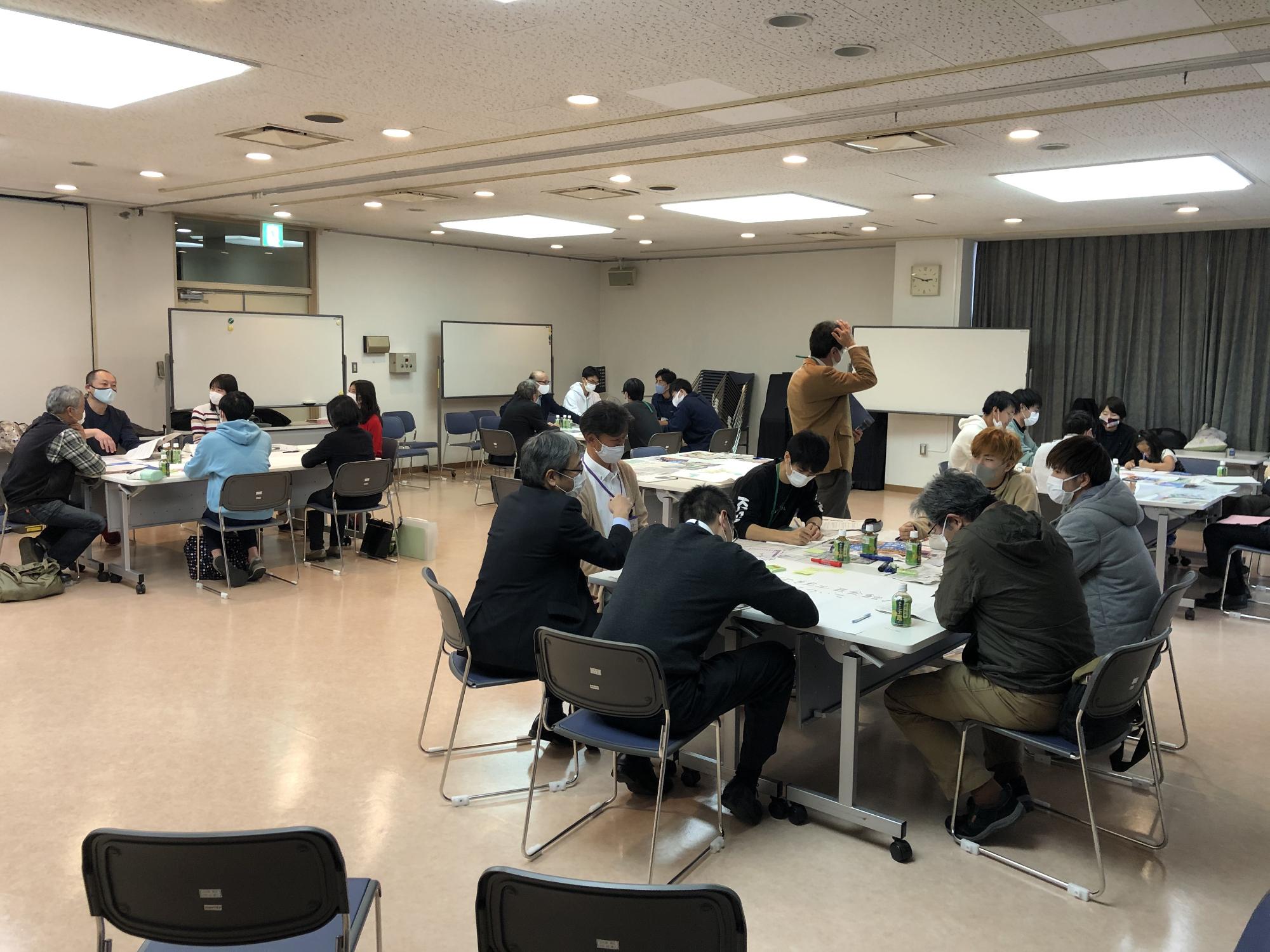 室内に4箇所に正方形の机が設置され各グループで話し合いをしている写真