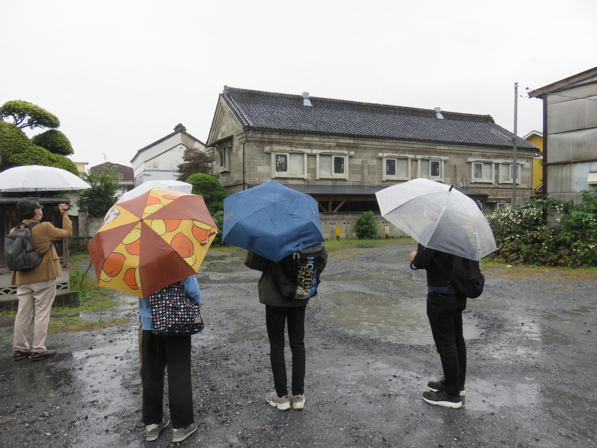 1名の方が傘をさしながら建物の写真をとり他の4名が立っているまち歩きの写真