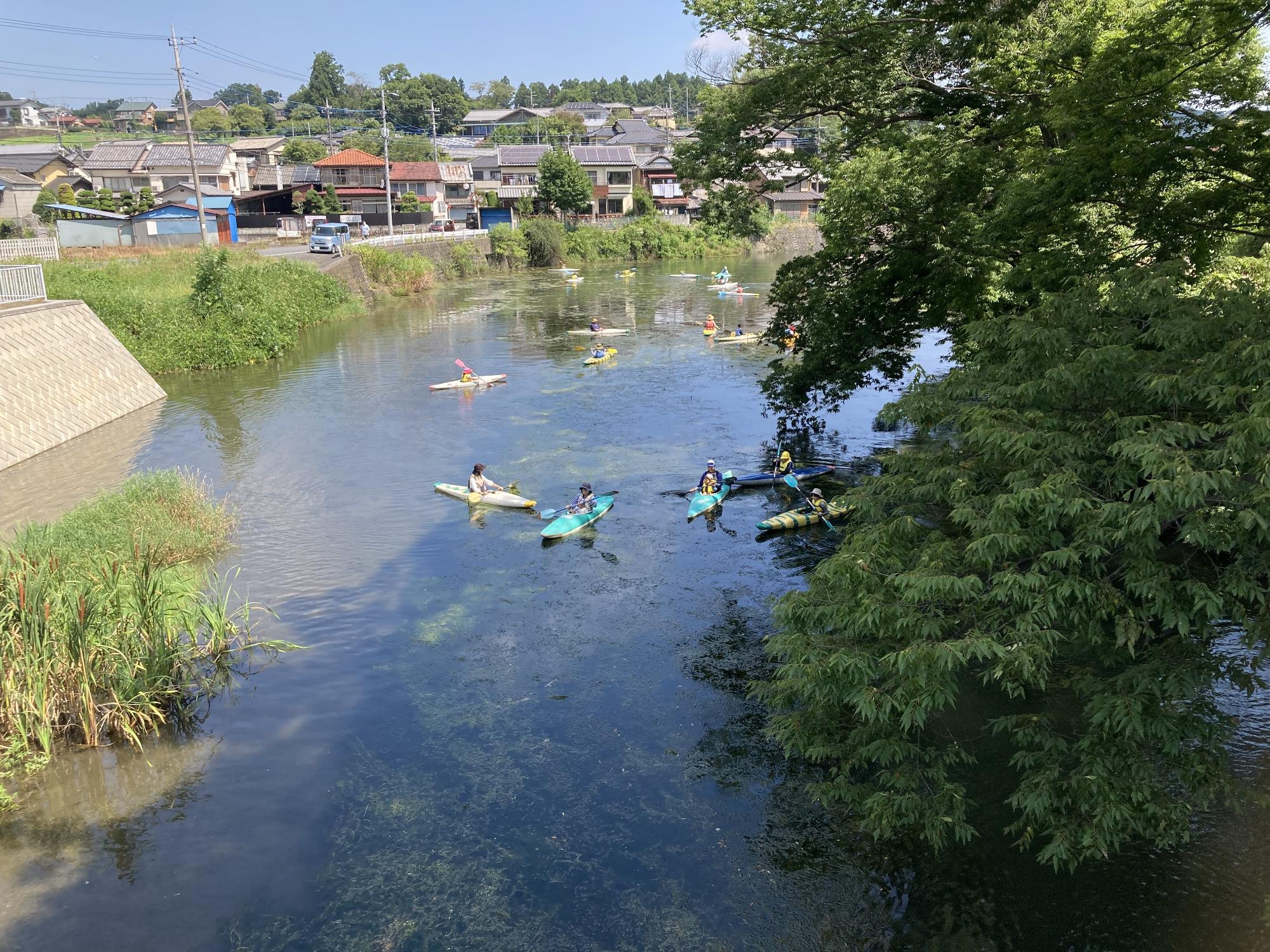 流れが穏やかな川でカヌーに乗っている参加者達を高い位置から撮影した写真
