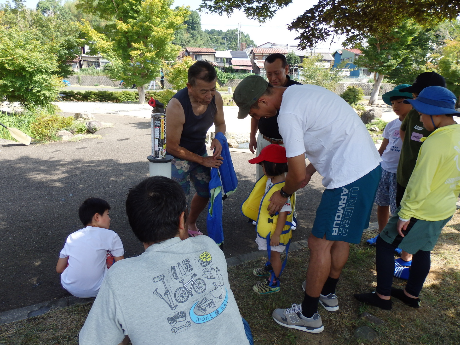 カヌー協会の男性が見守る中、お父さんが女の子にライフジャケットを着せている写真