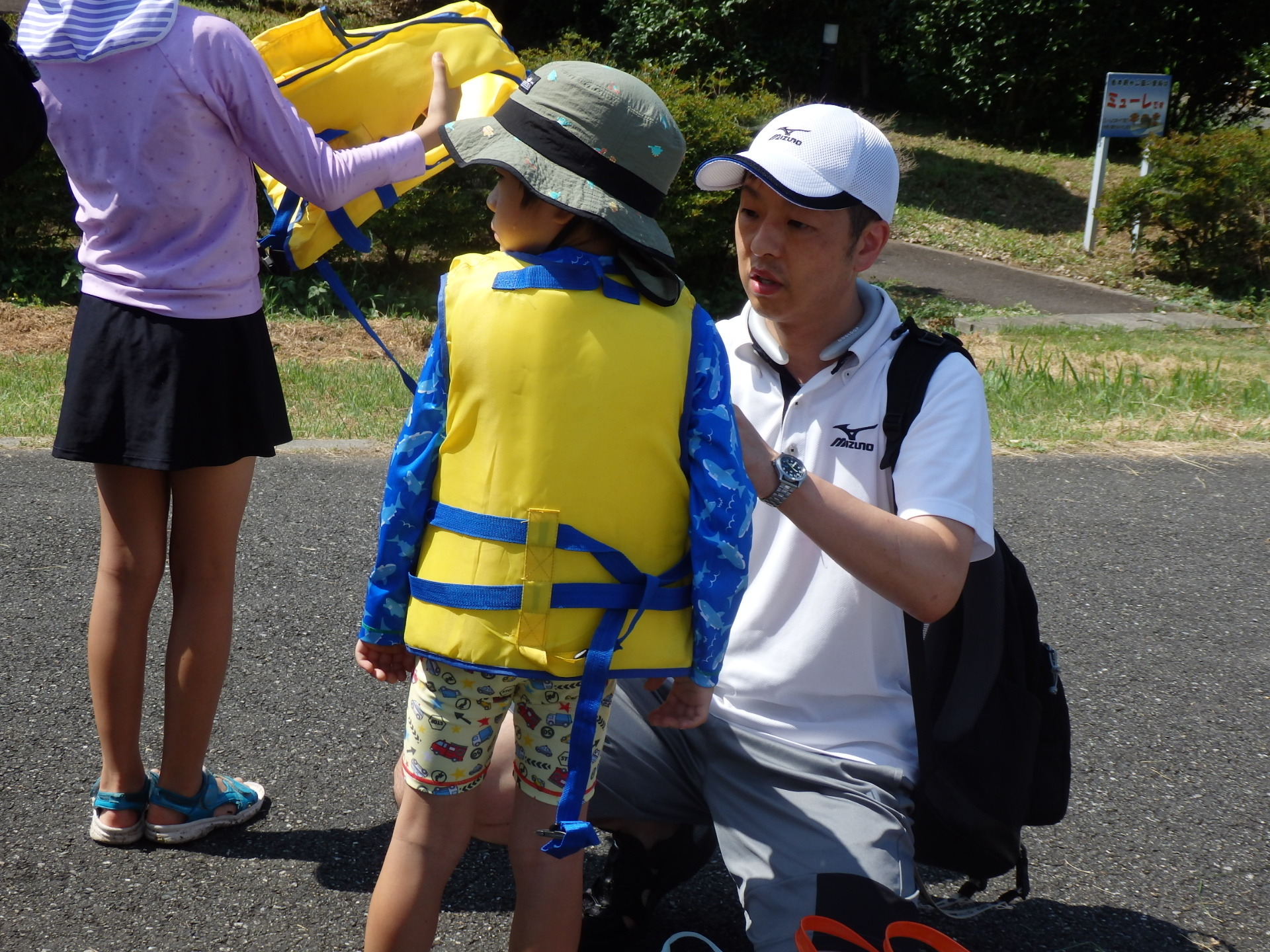 白いシャツを着たお父さんが男の子に黄色いライフジャケットを付けている写真