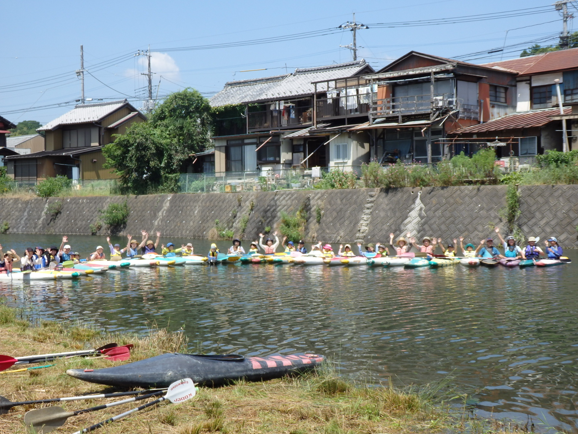川でカヌーに乗った参加者達が横一列になり、両手をあげて記念撮影をしている写真