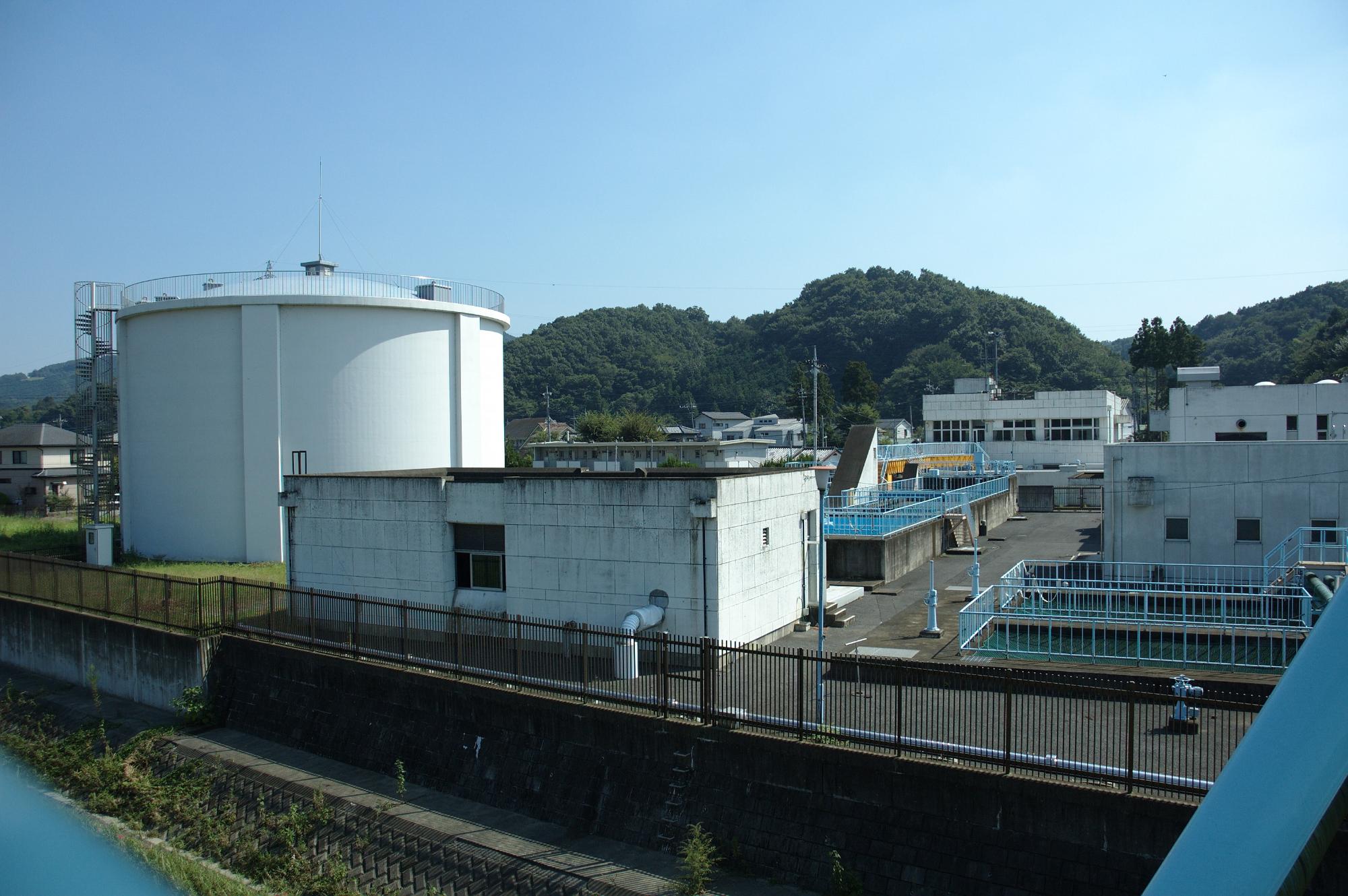 白い巨大なタンクと白い建物がある青山浄水場の写真