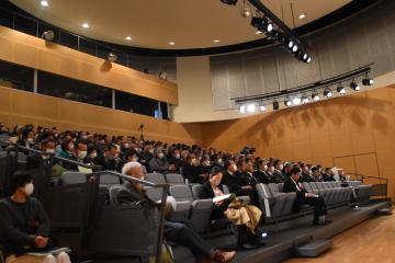 会場の席に座った多くの方々の様子を一列目の下から上にむかって斜めに撮影した写真