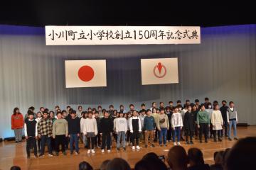 ステージ上に4列に並んだ児童たちが校歌を合唱する様子を前方から撮影した写真