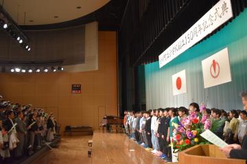 ステージ上の児童と観客の方々が向かい合っている様子を横から撮影した写真