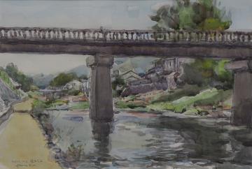 川沿いに民家が建ち並ぶ風景を、橋の下を通る遊歩道から描いた逸見 章さんの作品