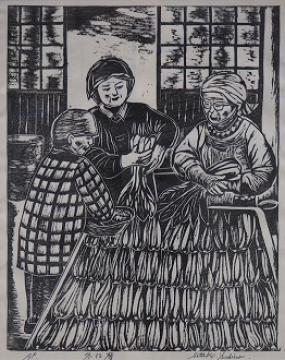 頭に布を巻いて作業している3人の女性たちが葉物の野菜を箱に並べて冬支度する様子の吉野 節子さんの木版画の作品