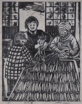 男性と2名の女性が四角形の大きなザルの様なものに収穫した野菜を並べている様子を木版画で描いた吉野 節子さんの作品