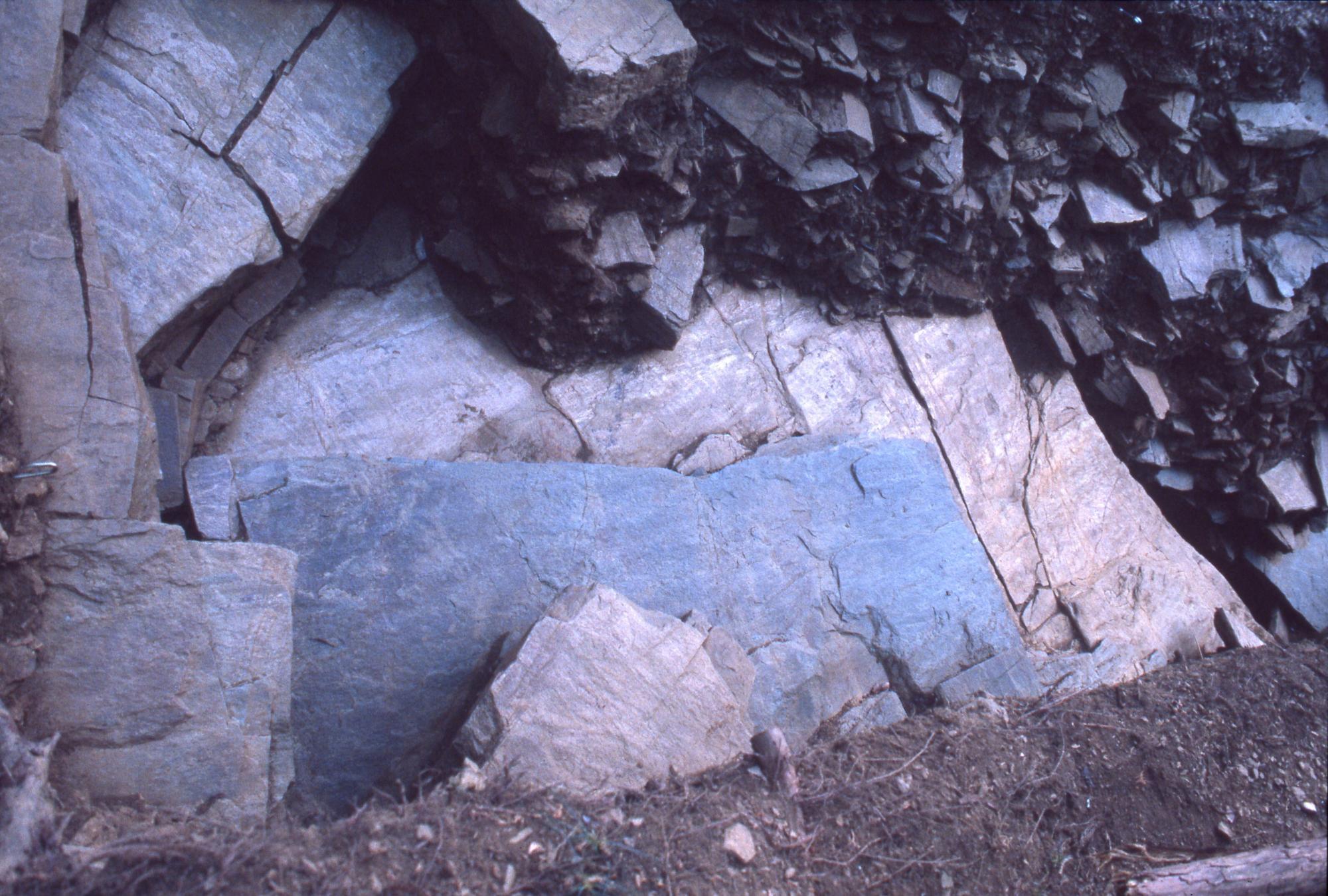 土の中から黒っぽい石と灰色やクリーム色の大きな板状の石が折り重なっている様子を南側より上から撮影した写真